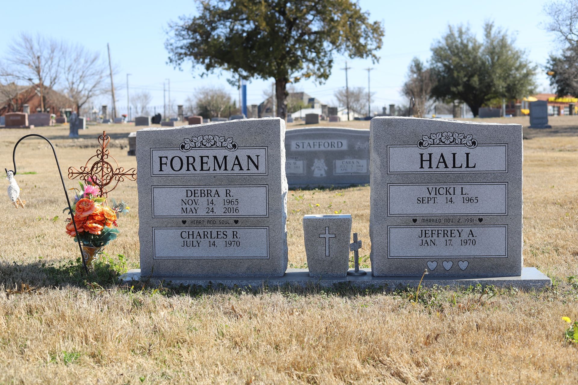 Gravestone markers in a cemetery; two with the surnames Foreman and Hall, with flowers in front.