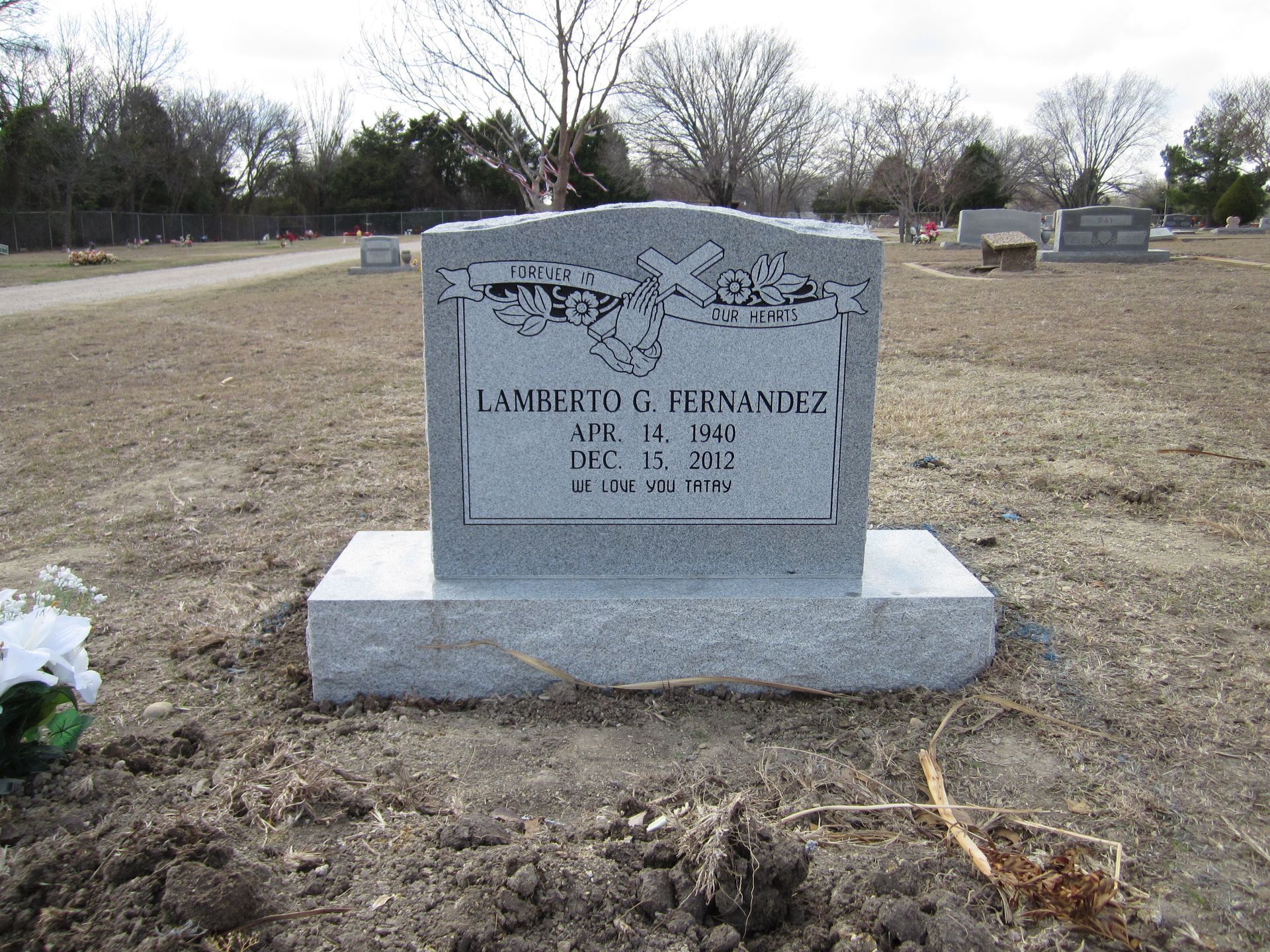 Headstone in a cemetery with a name, dates, and decorative carvings.