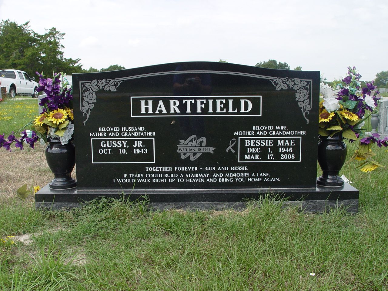 Black granite headstone with floral arrangements, HARTFIELD engraved at top; names and dates visible.