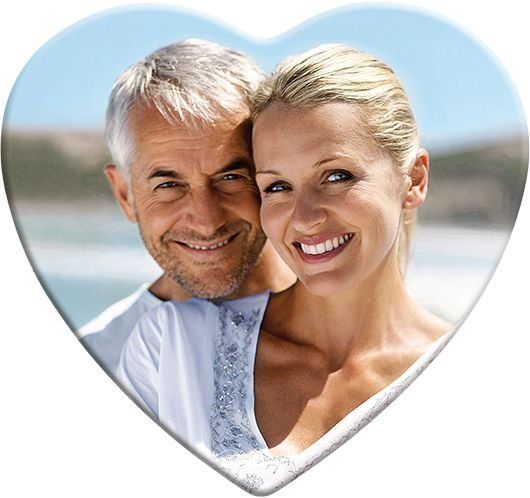 Couple smiling, embracing in heart-shaped frame, blue sky background.