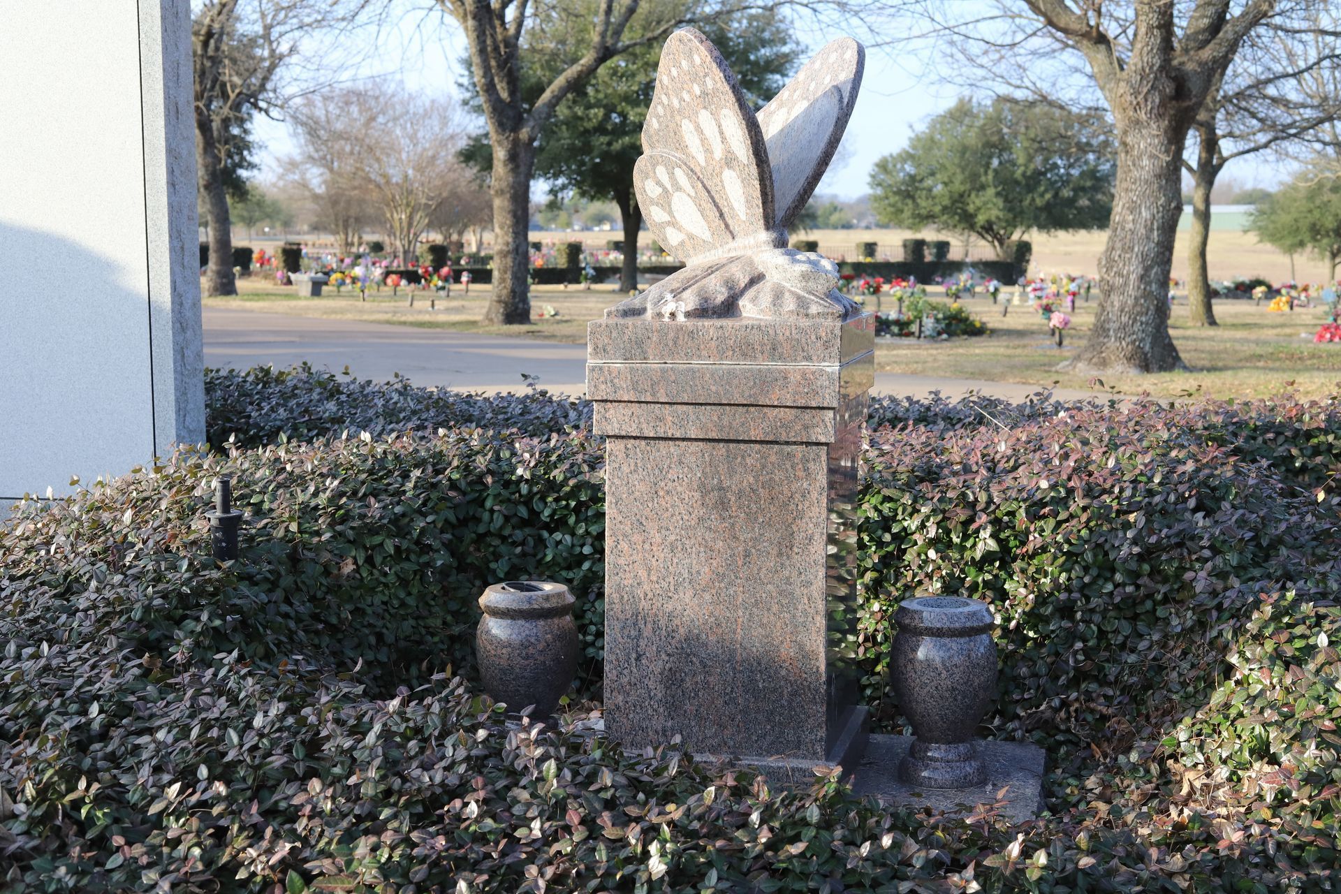 Stone butterfly sculpture with two urns in a cemetery.