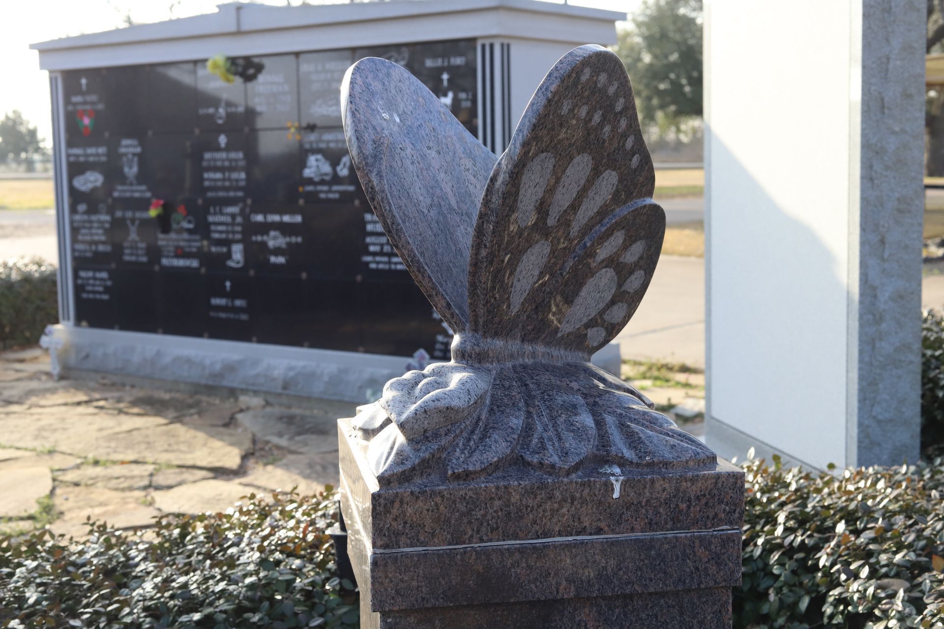 Butterfly headstone in a cemetery with a black columbarium in the background.