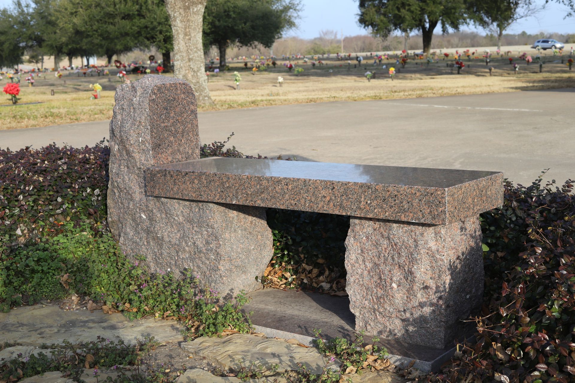 Stone bench in a cemetery, with a granite seat and rough stone supports, set among bushes.