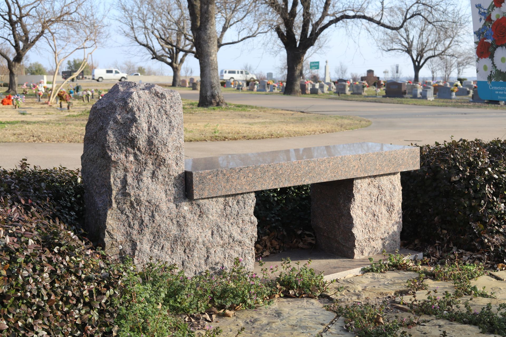 Stone bench in a cemetery with a background of headstones and trees.