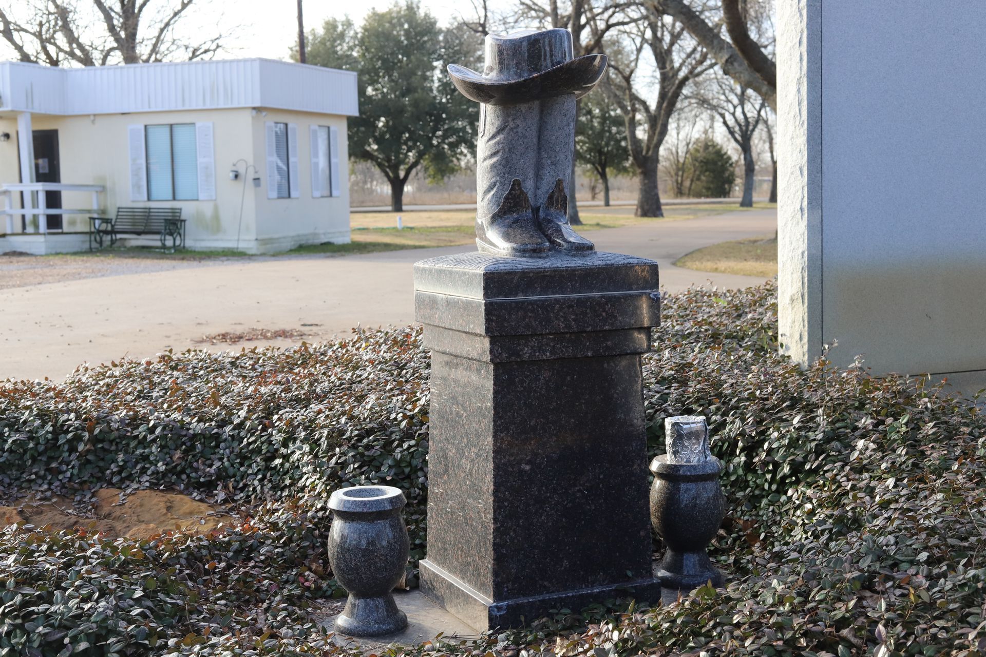 Black granite monument shaped like cowboy boots and hat; two urns sit at base.