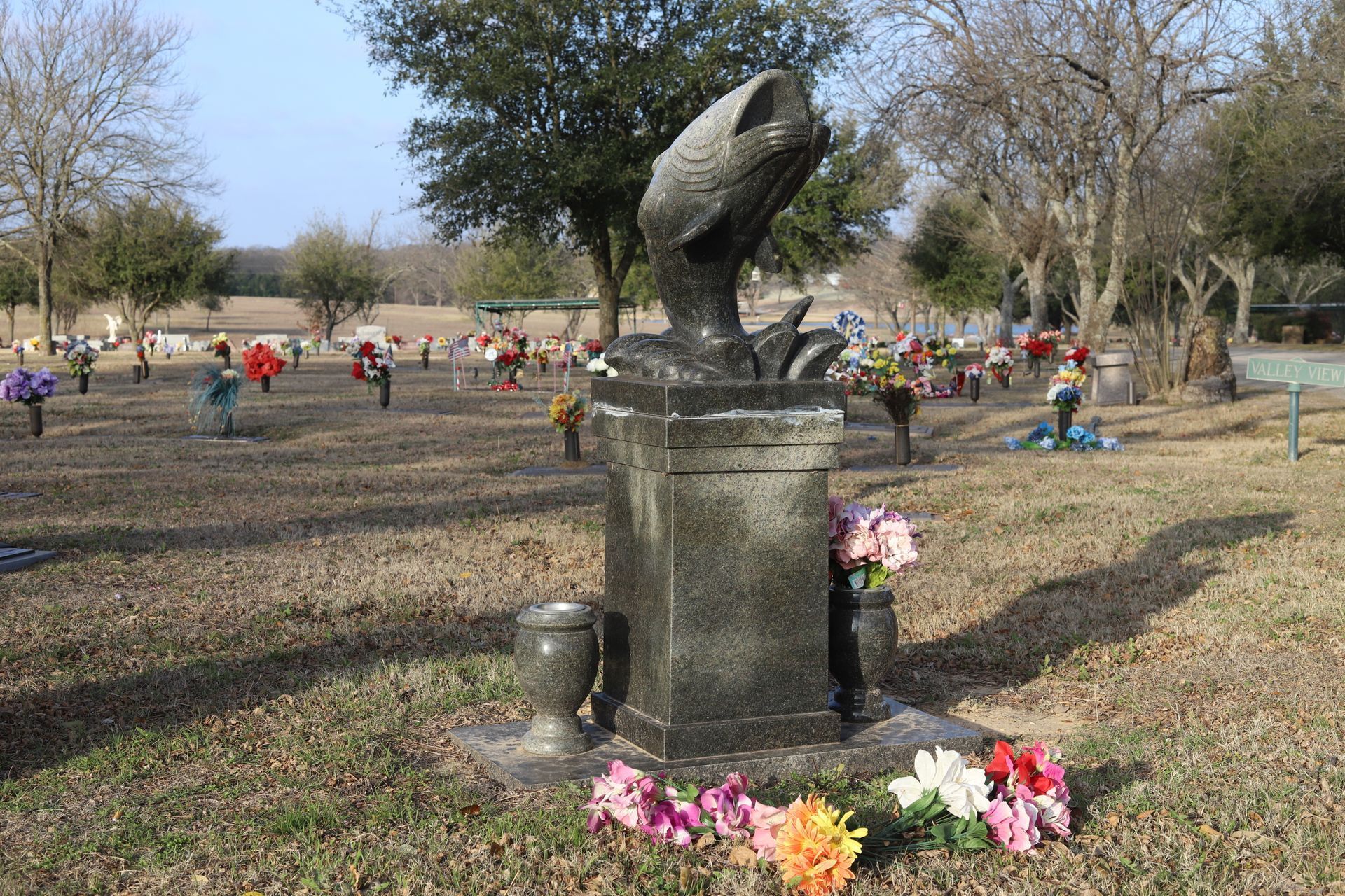Grave with sculpted fish and flowers in a cemetery on a sunny day.
