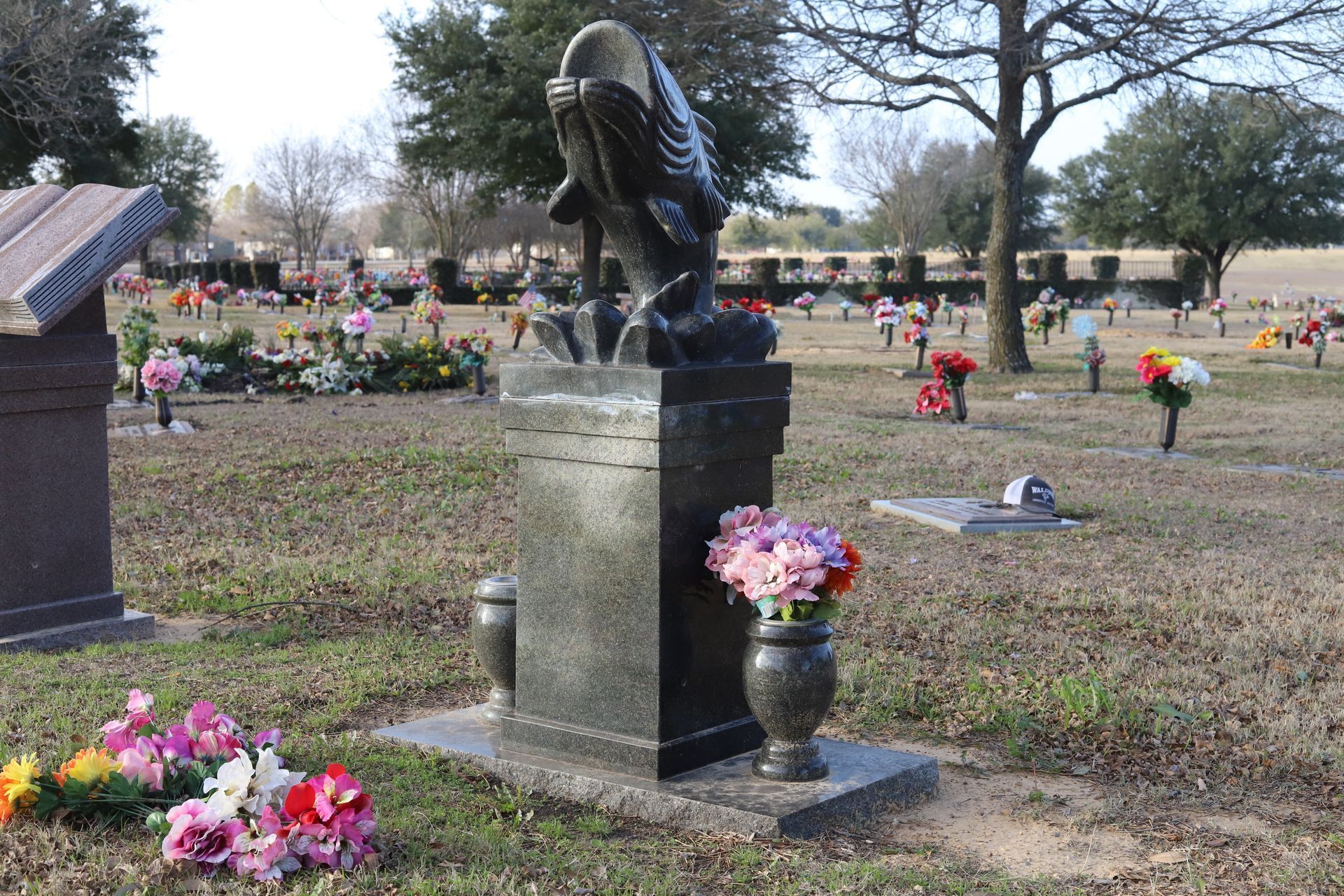 Grave in a cemetery with a black granite monument topped with an eagle statue, surrounded by flowers.