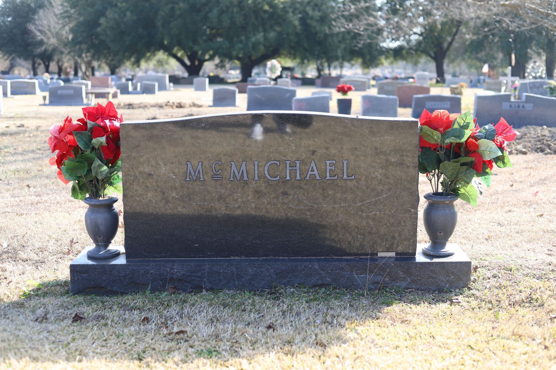 Headstone in a cemetery with red floral arrangements in vases. Name: M. McMichael.