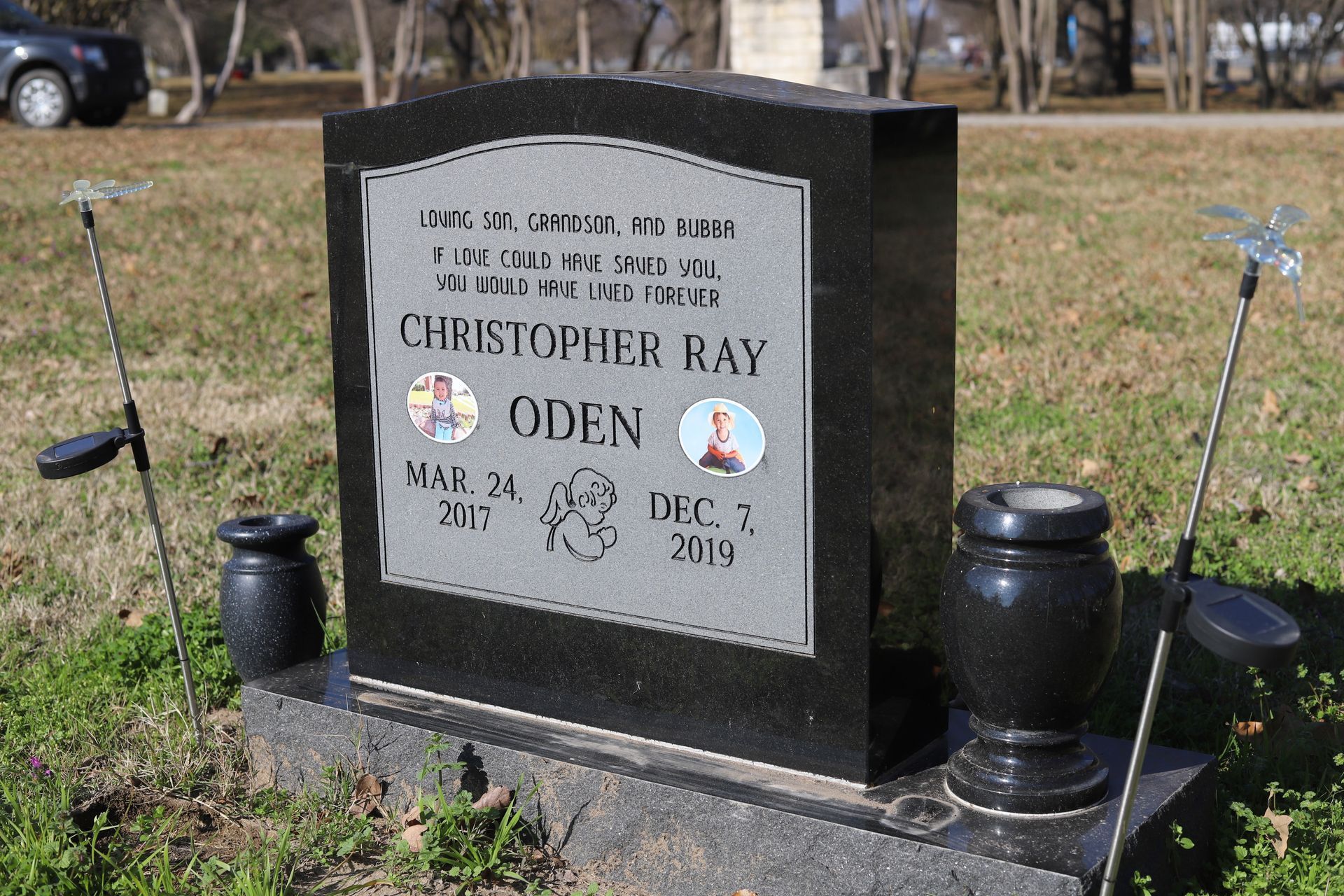 Black granite headstone with photo insets and dates in a grassy cemetery.