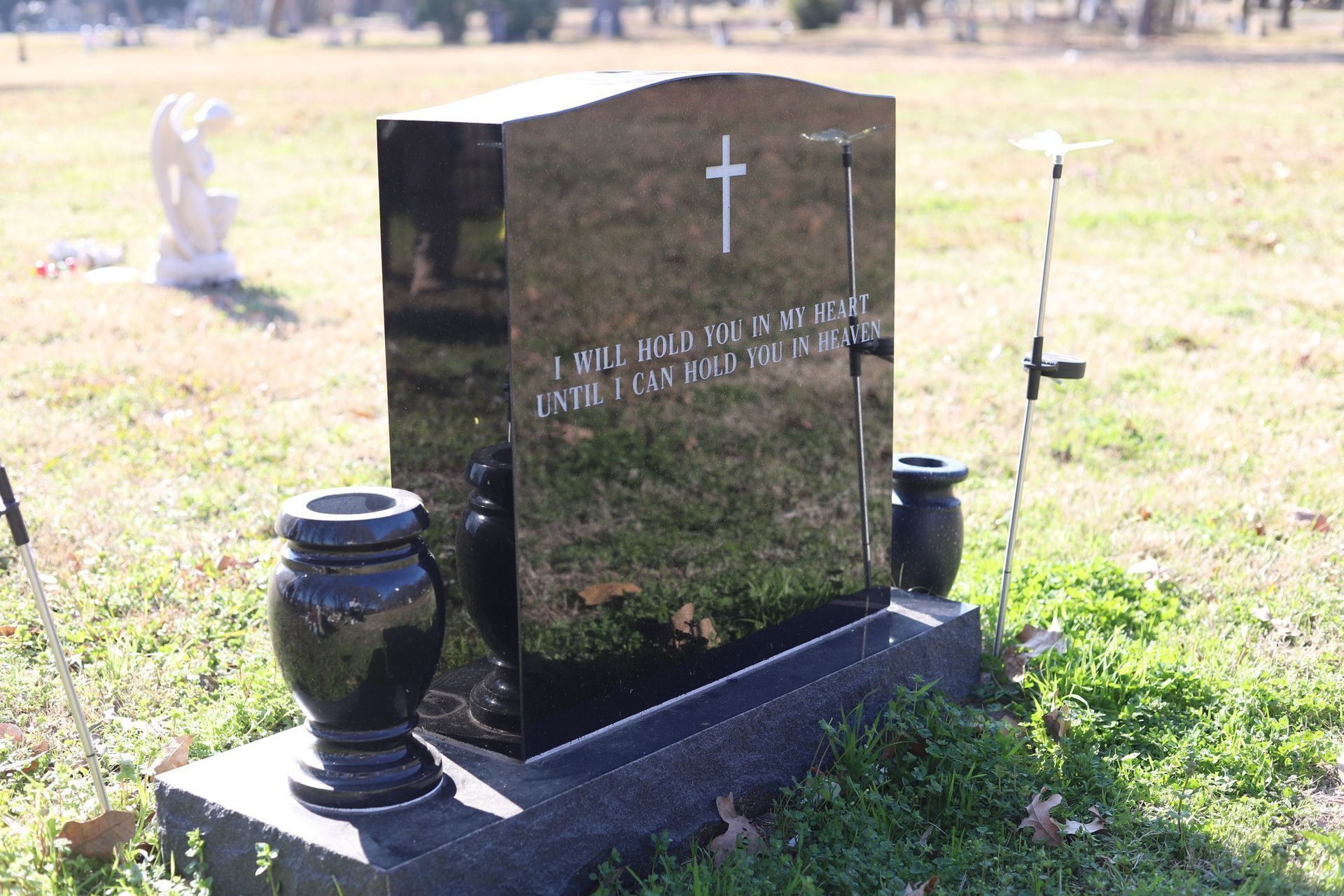 Black headstone with a cross and inscription in a grassy cemetery.