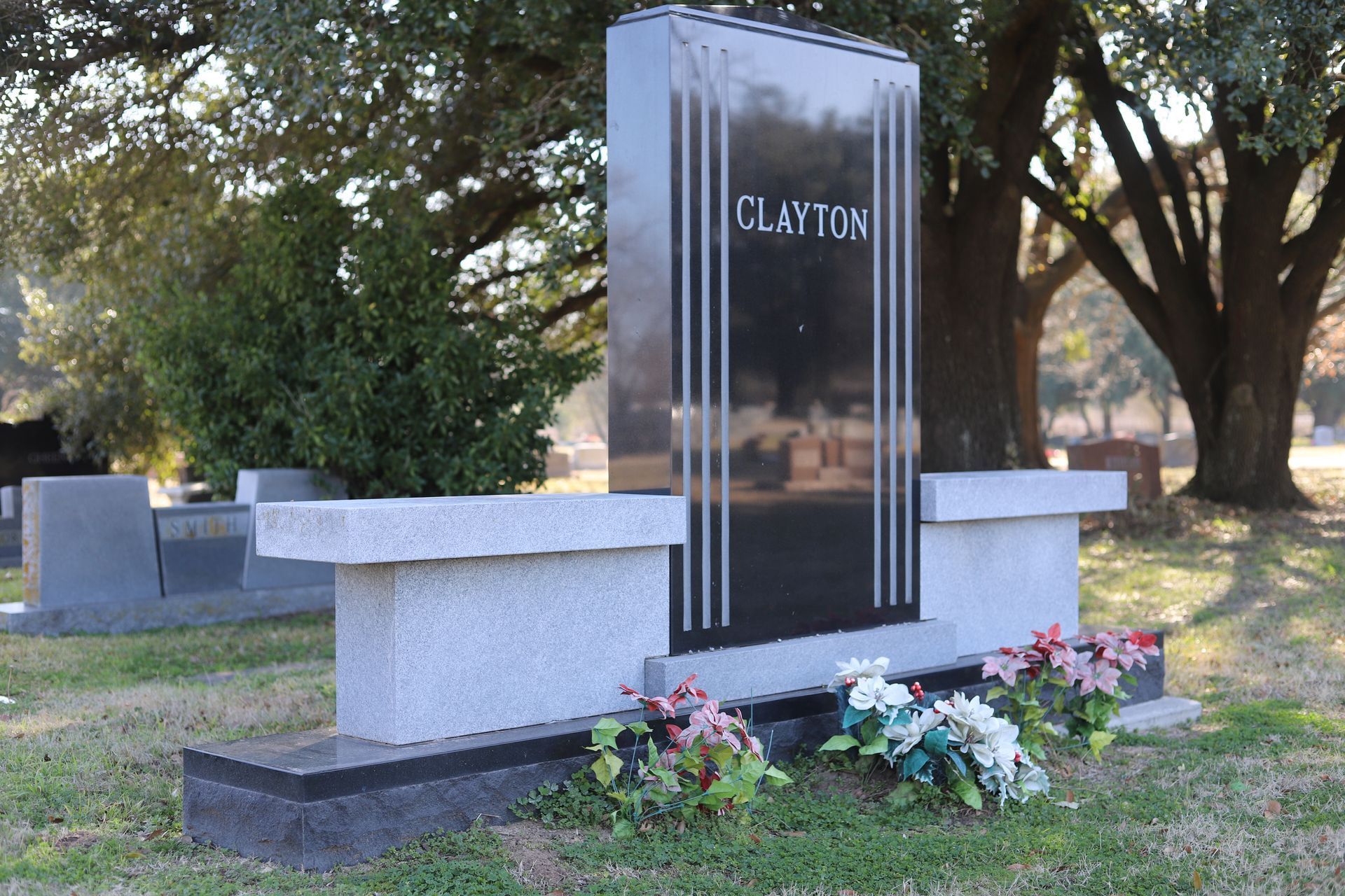 Grave marker in a cemetery, featuring a tall, dark stone with the name 