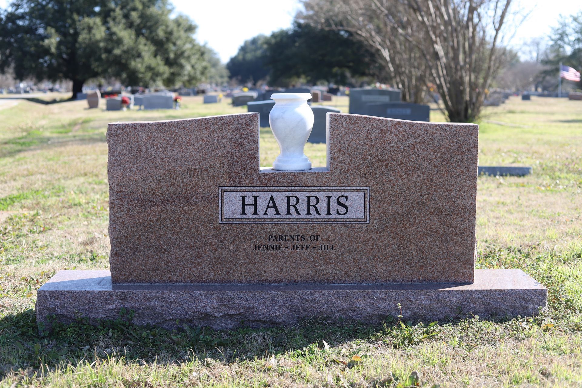 Brown granite tombstone in a cemetery with a white vase, the name