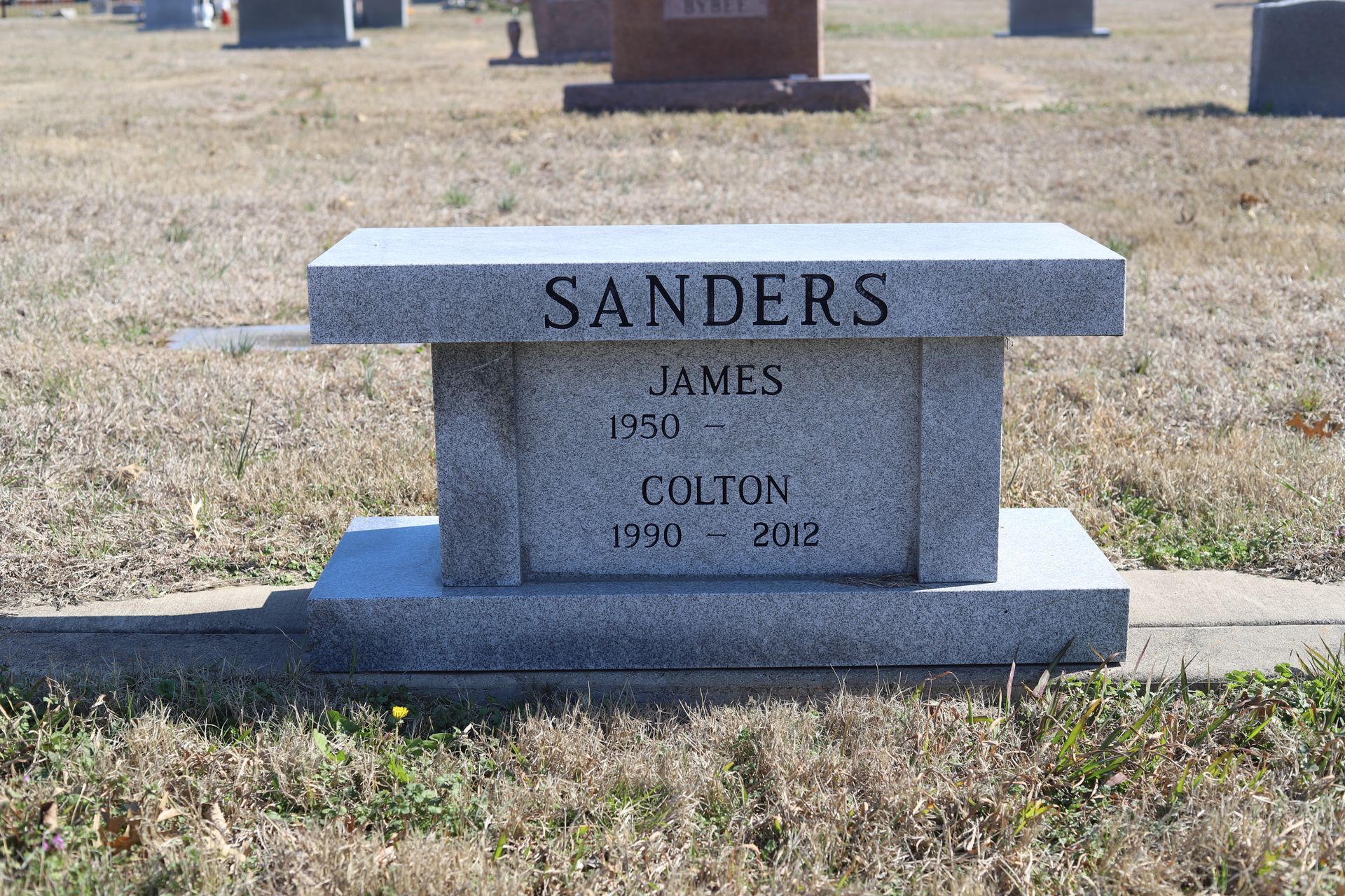 Gray stone bench headstone in a cemetery; reads 