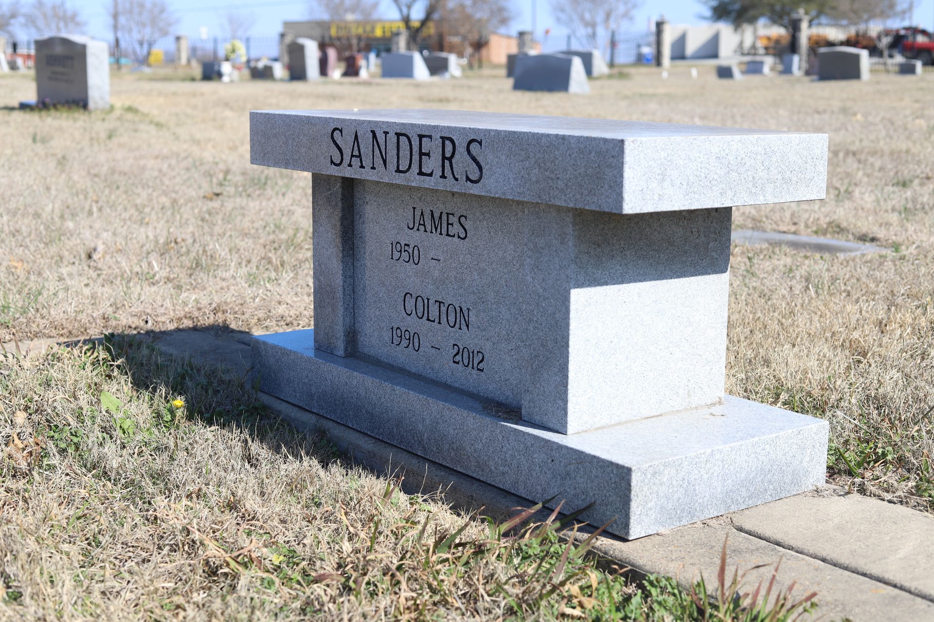 Gray granite bench-style tombstone in a cemetery; reads 