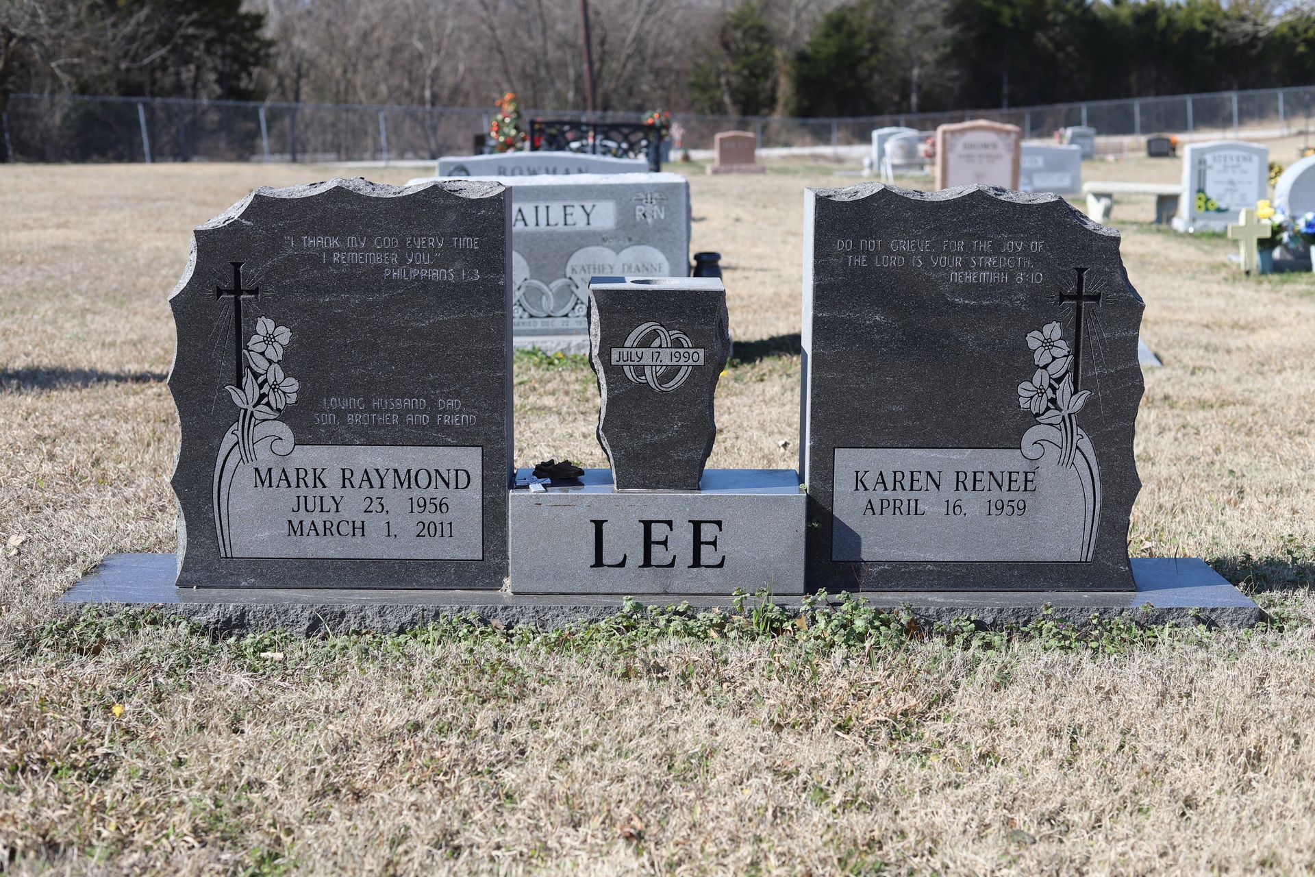 Grave markers in a cemetery. Two upright granite headstones flank a smaller, central marker.