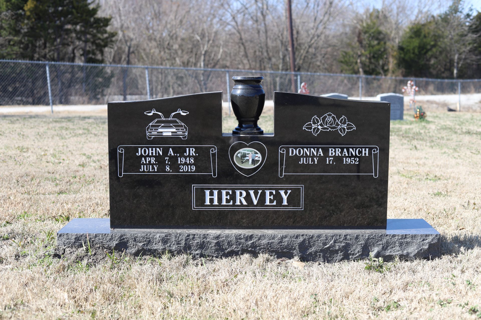 Black granite headstone with vase, names, and dates, in a cemetery.