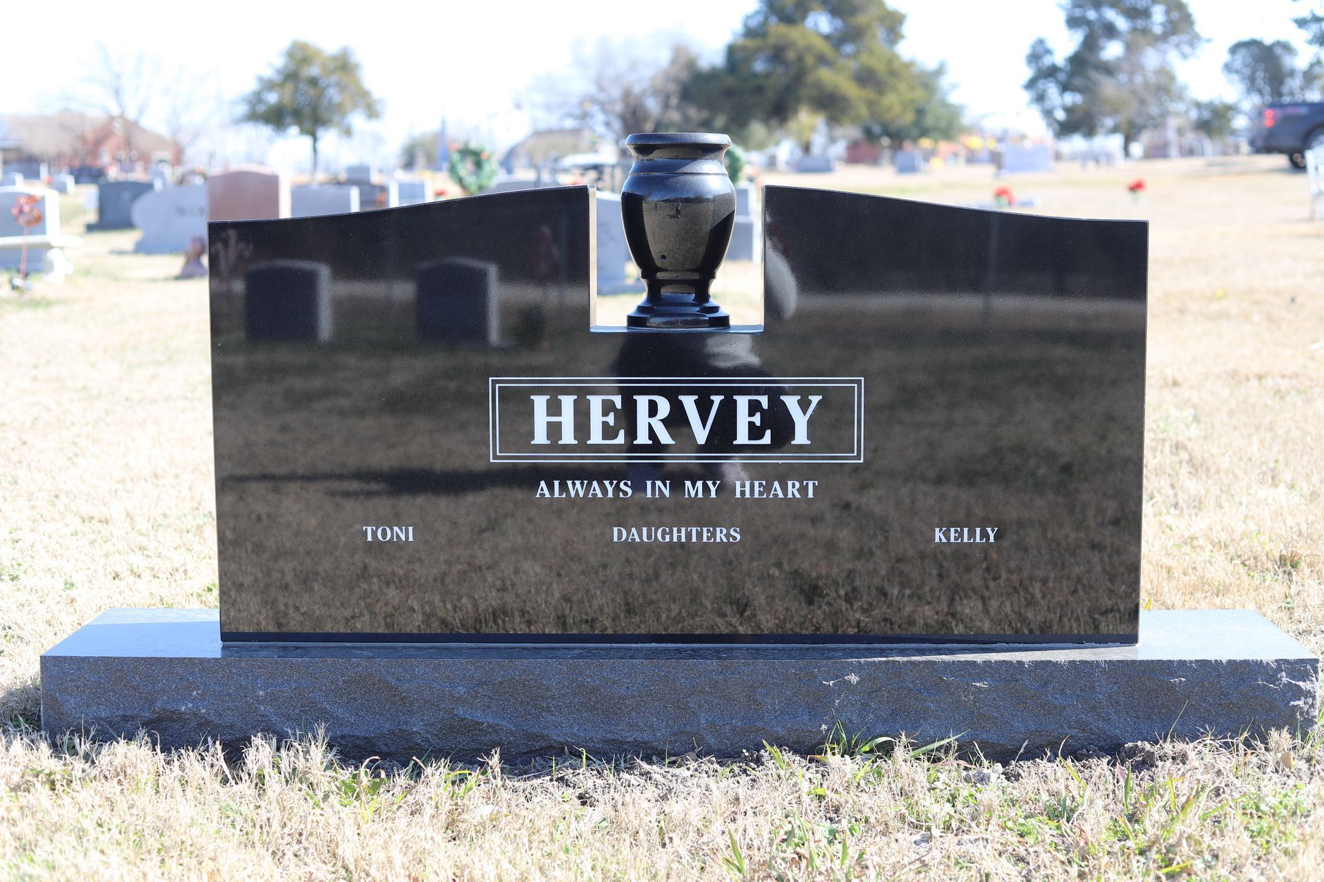 Black granite headstone in a cemetery with a vase, name