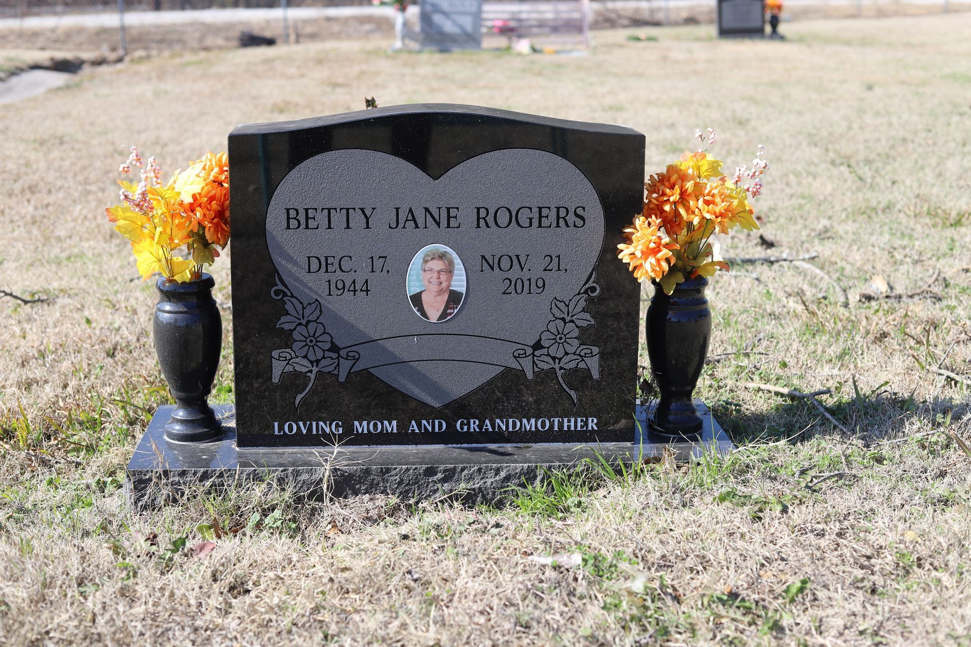 Black granite tombstone with floral arrangements. Reads