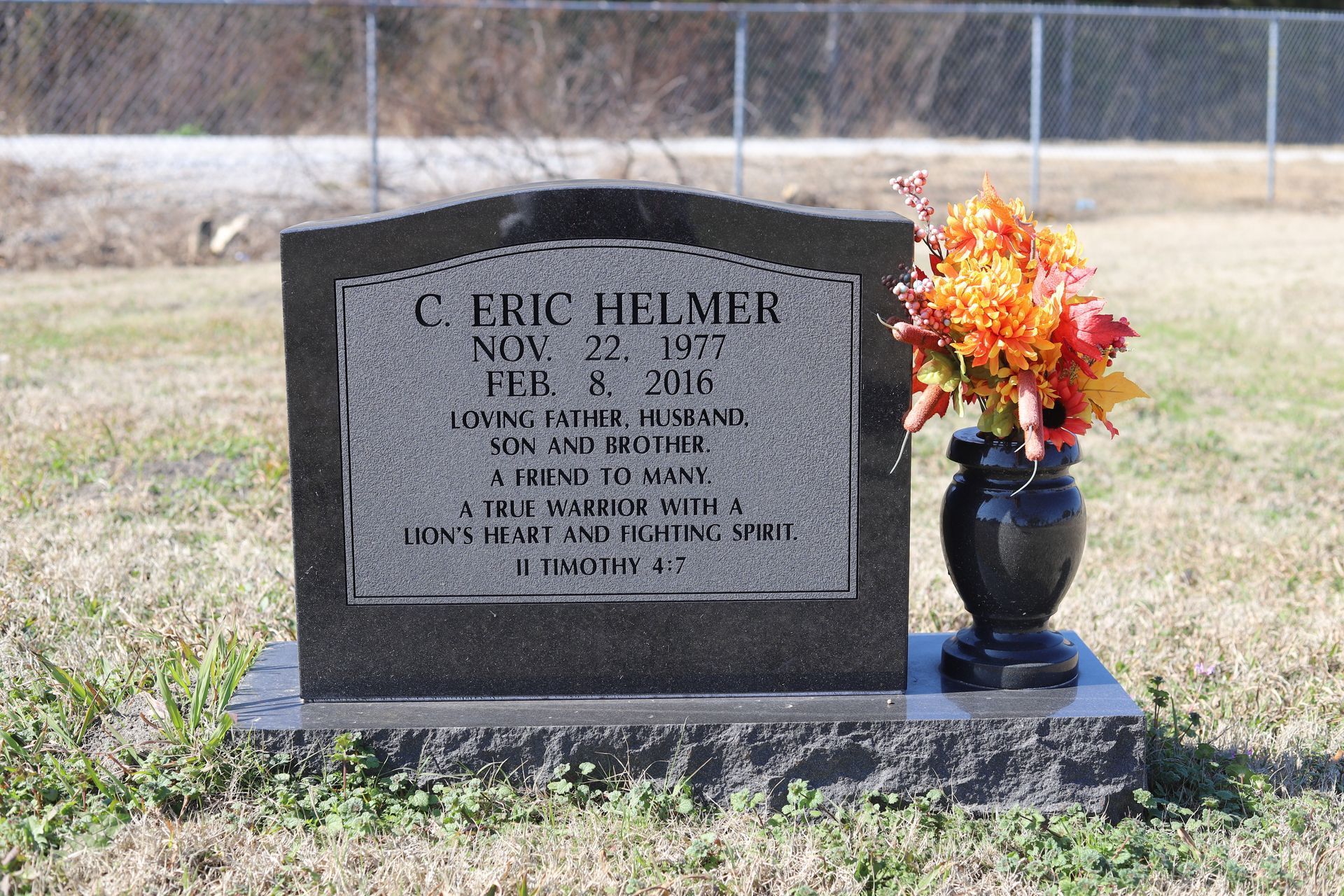 Headstone for C. Eric Helmer, with birth/death dates, inscription, and a vase of orange flowers.