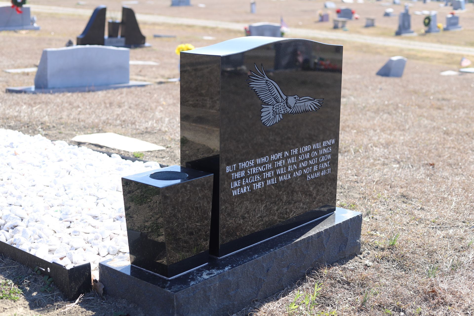 Black granite headstone with eagle engraving, text, and attached vase, in a cemetery.