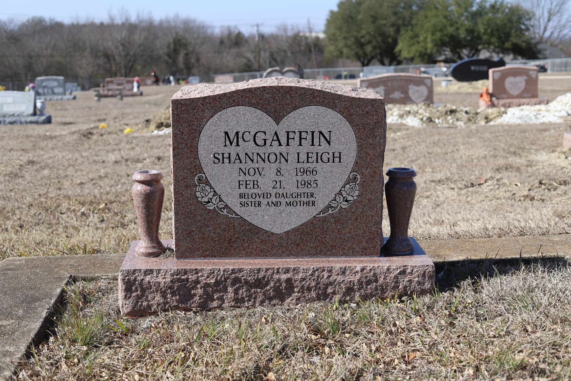 Gravestone with heart design, red-toned granite. Name: McGaffin, Shannon Leigh. Cemetery setting.