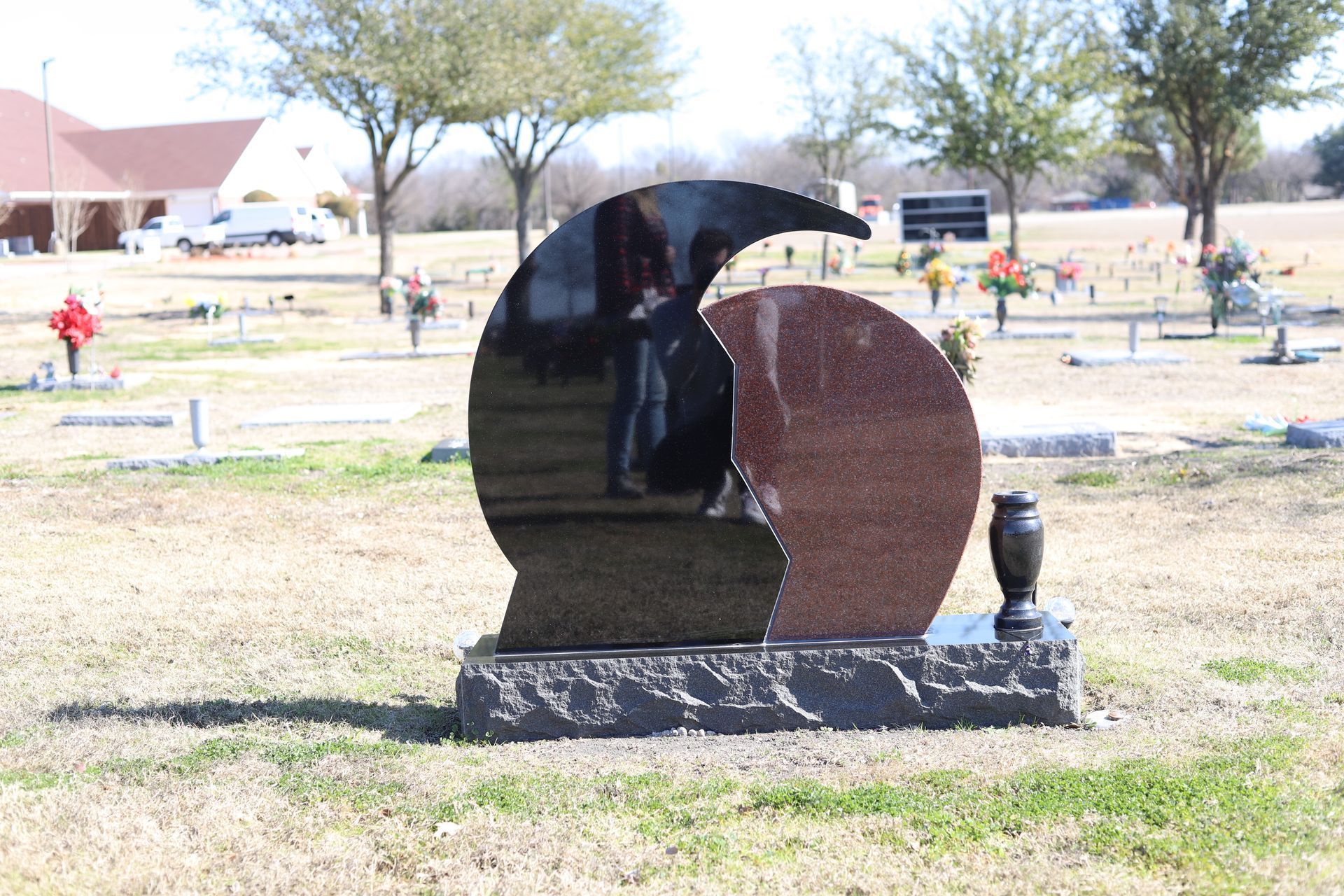 Black and red granite headstone with a unique curved shape in a cemetery.