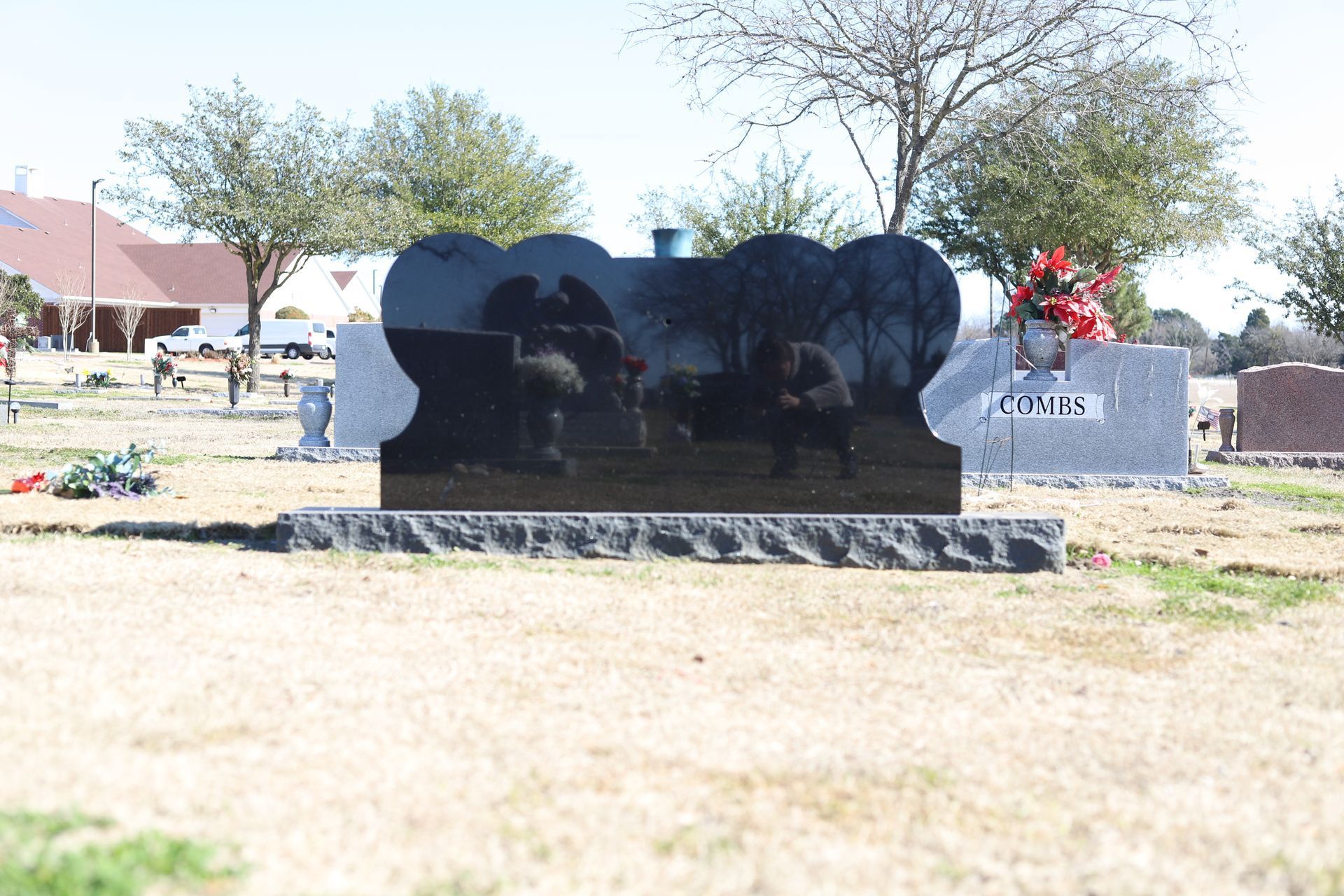 Black tombstone in a cemetery with a floral arrangement.