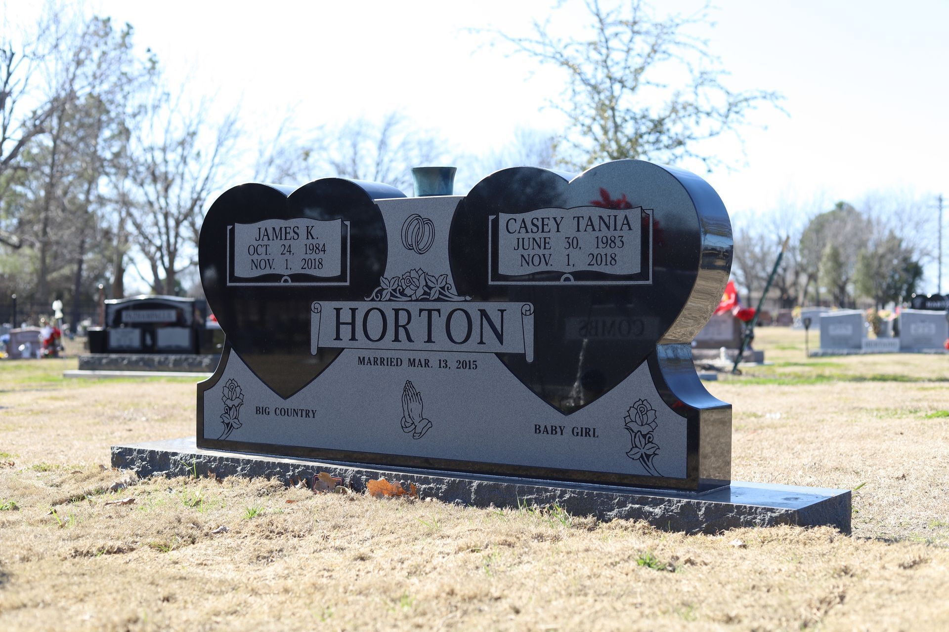 Black heart-shaped headstone with names and dates in a cemetery.