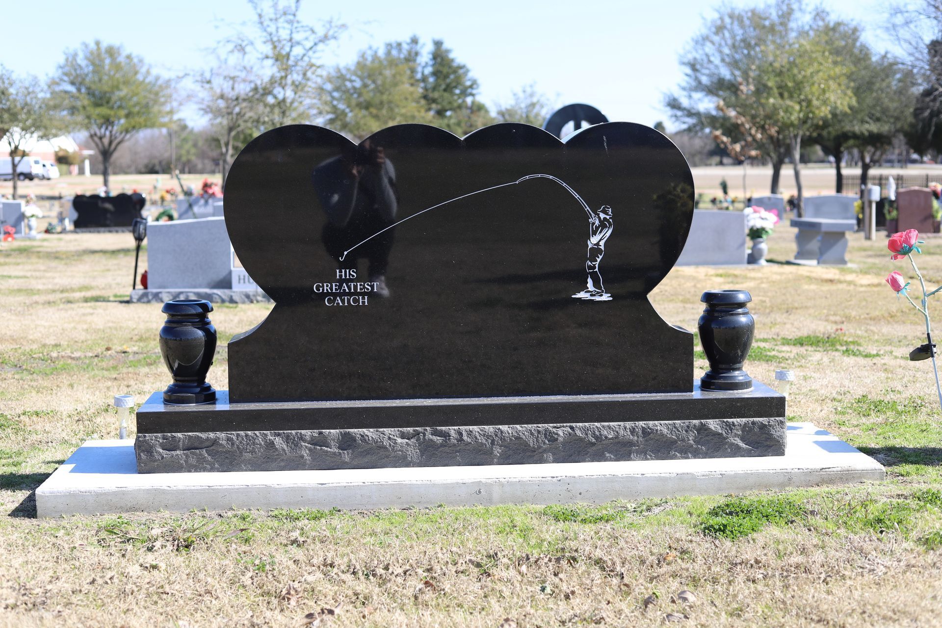 Black granite tombstone with fishing scene in a cemetery.