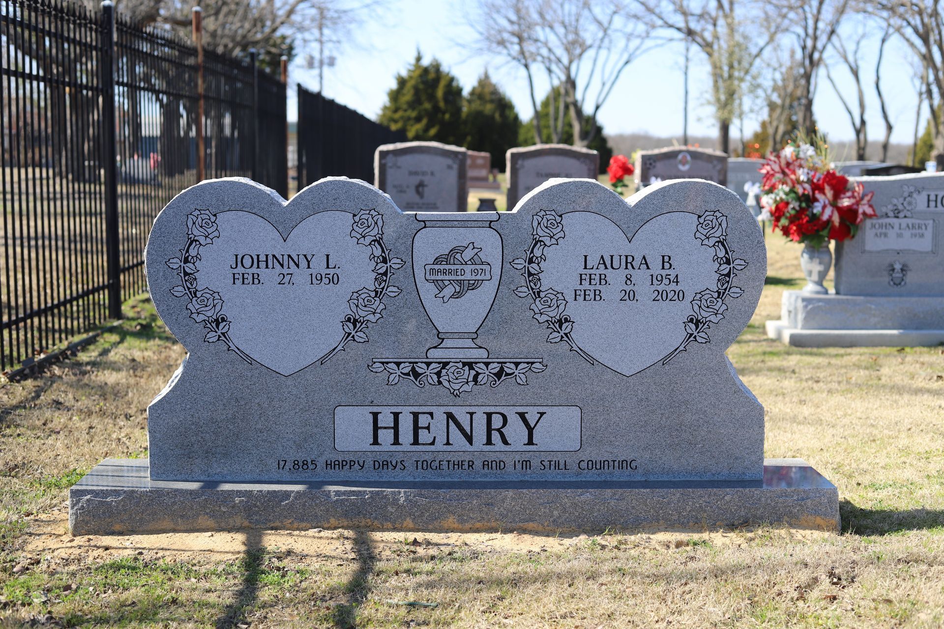 Gray headstone in a cemetery; heart-shaped panels with names, dates, and 
