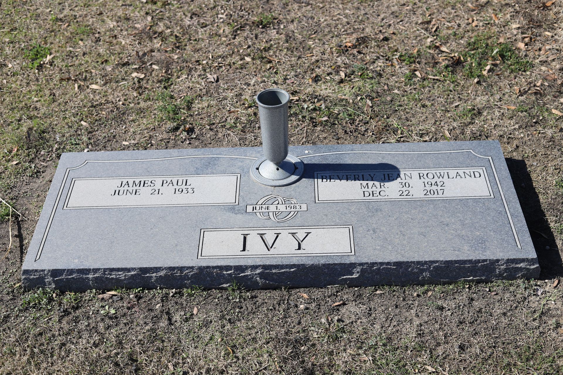 Gray granite tombstone with two name plates, a vase holder, and the name 
