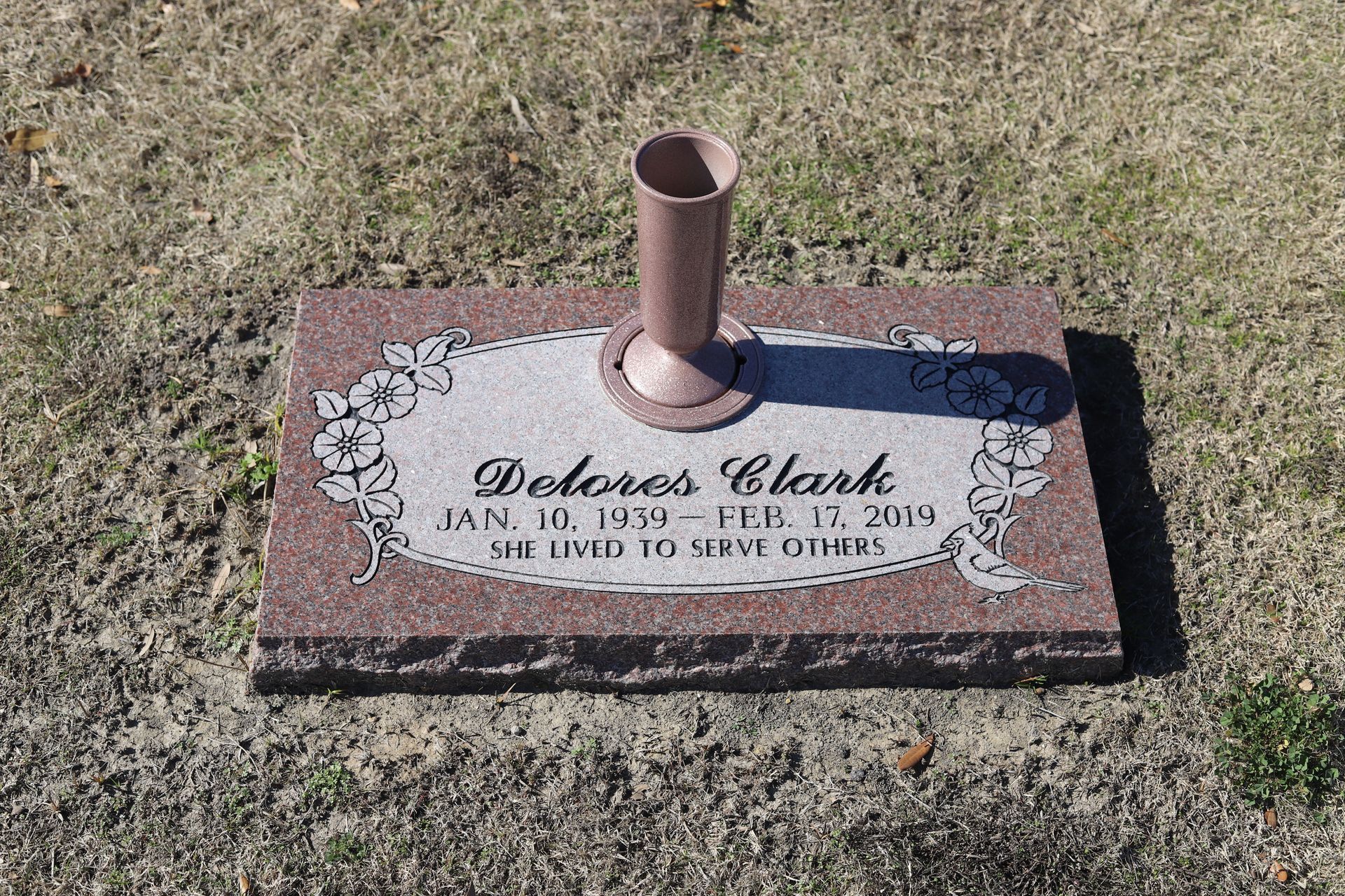 Headstone of Dolores Clark, with birth and death dates, and a vase, in a grassy setting.