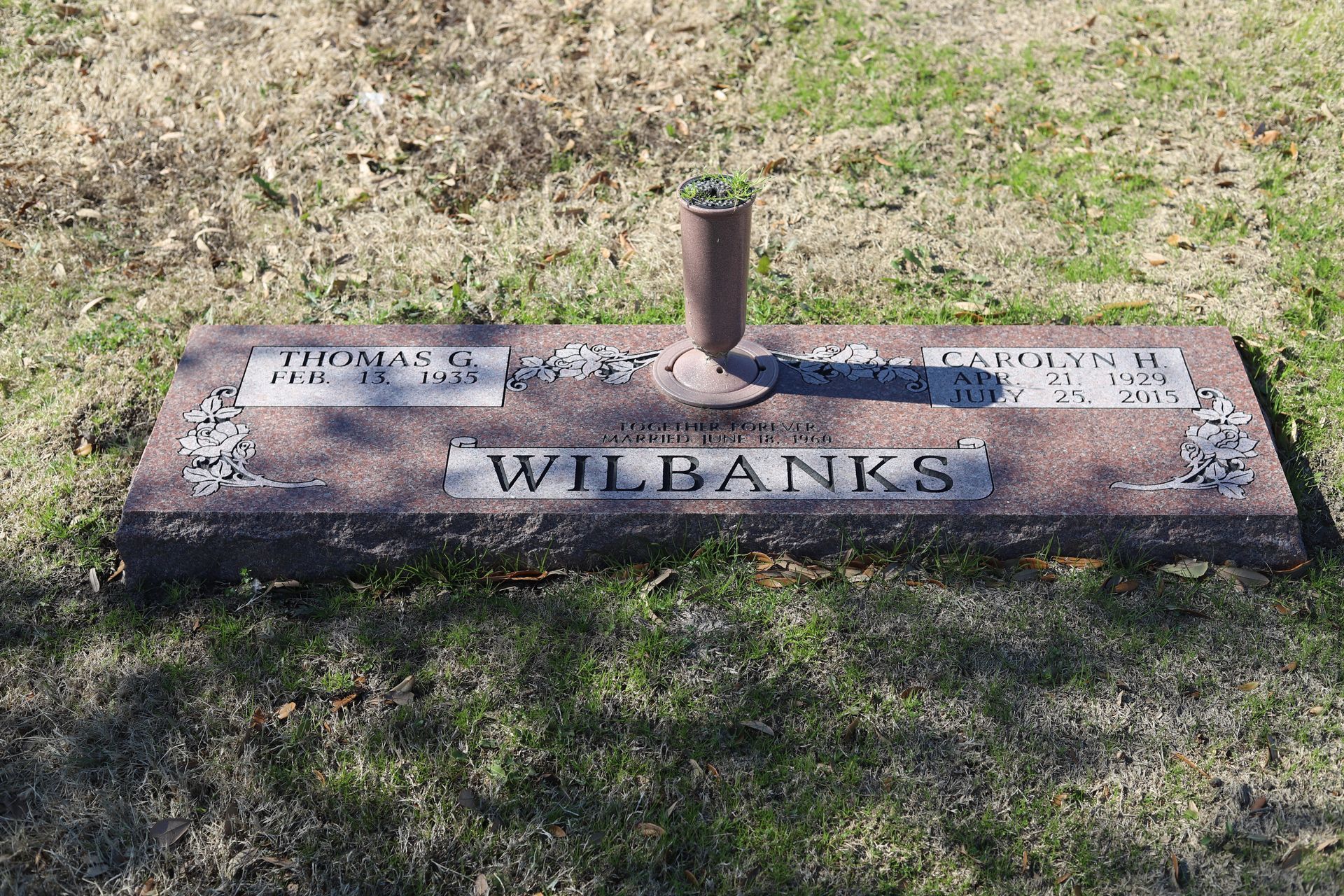 A grave marker for the Wilbanks family, brown granite, with names and dates, and a metal vase.