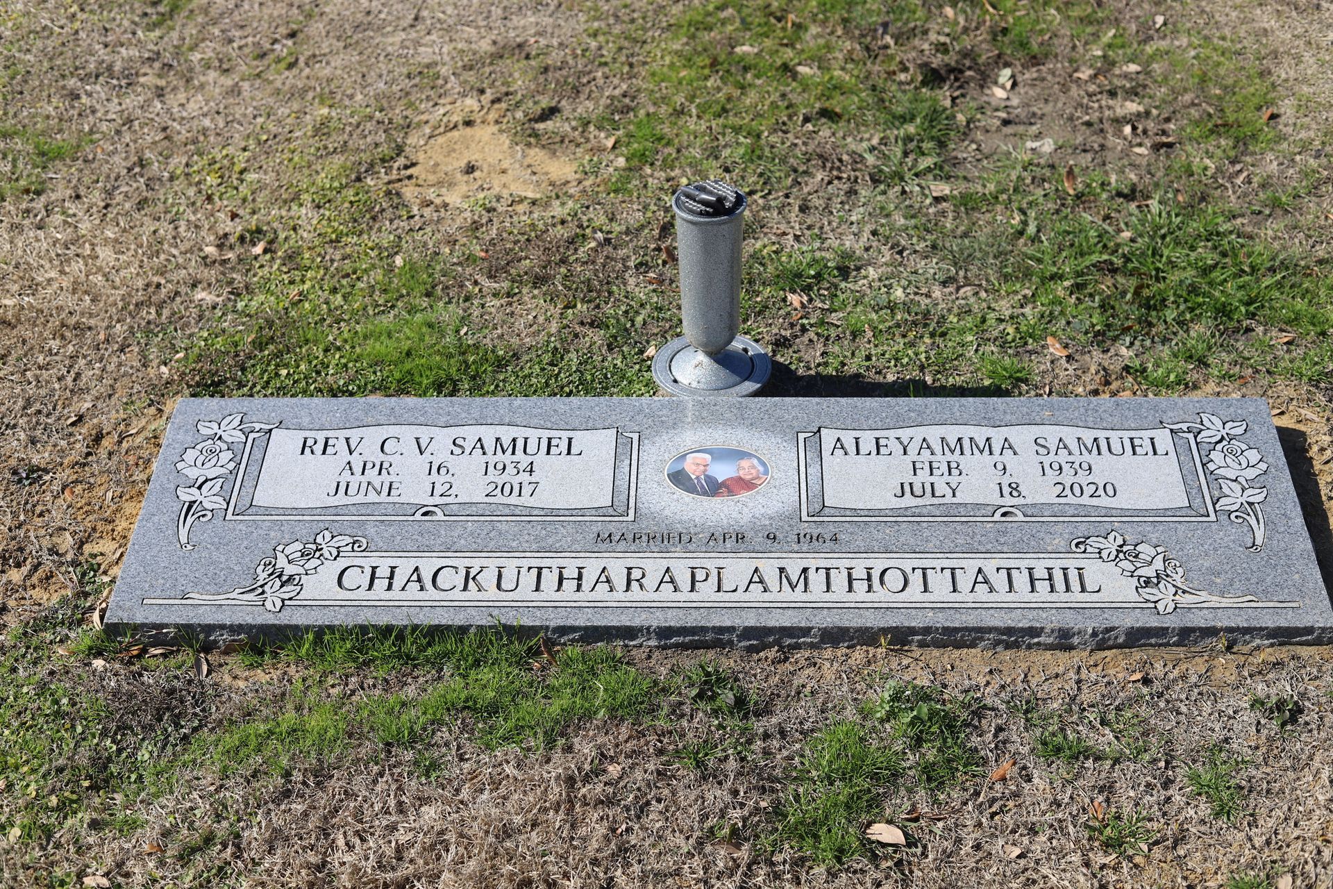Gravestone with two name plaques, a floral emblem, and a vase, set in grass.