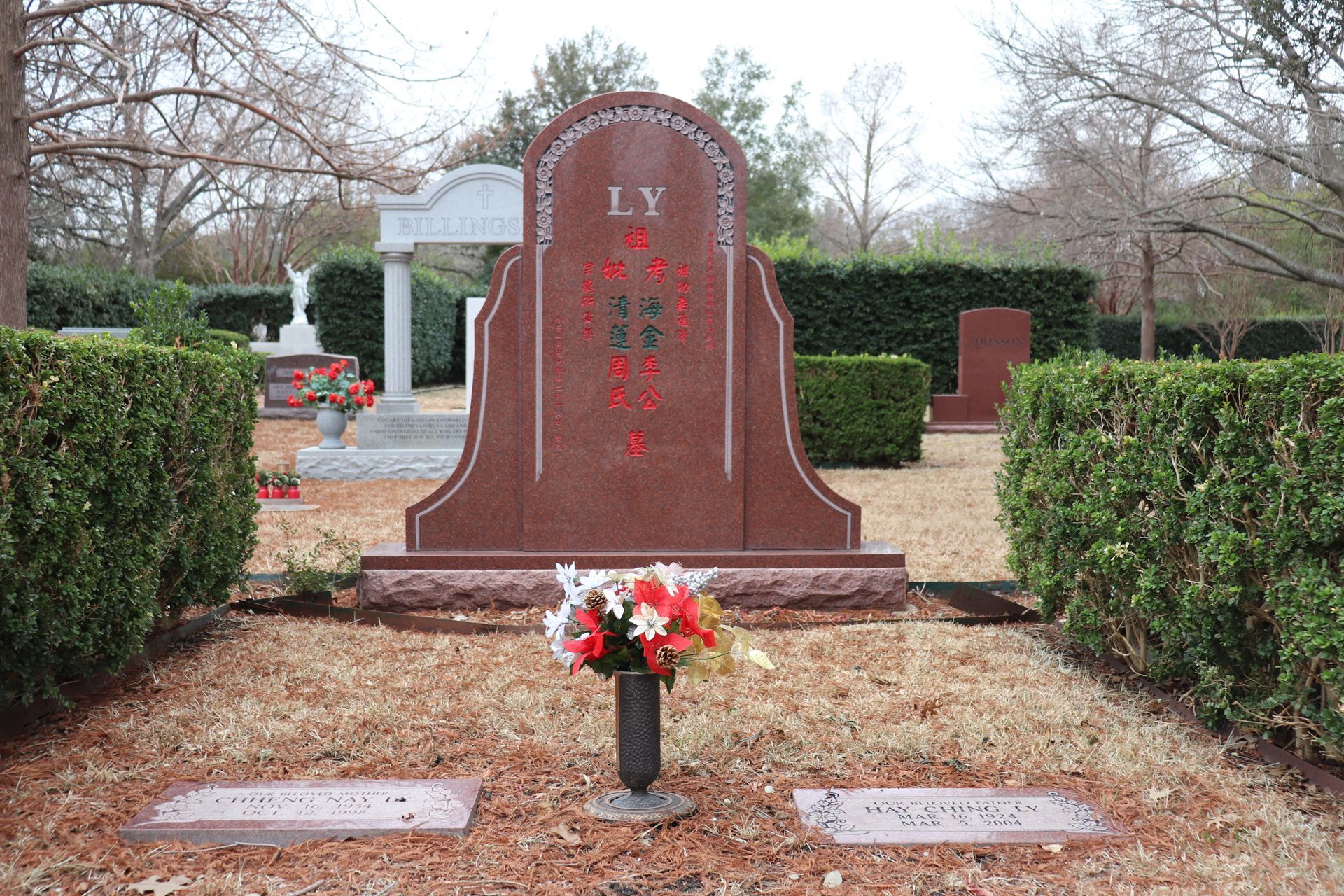 Red granite tombstone in a cemetery with a flower vase in front.