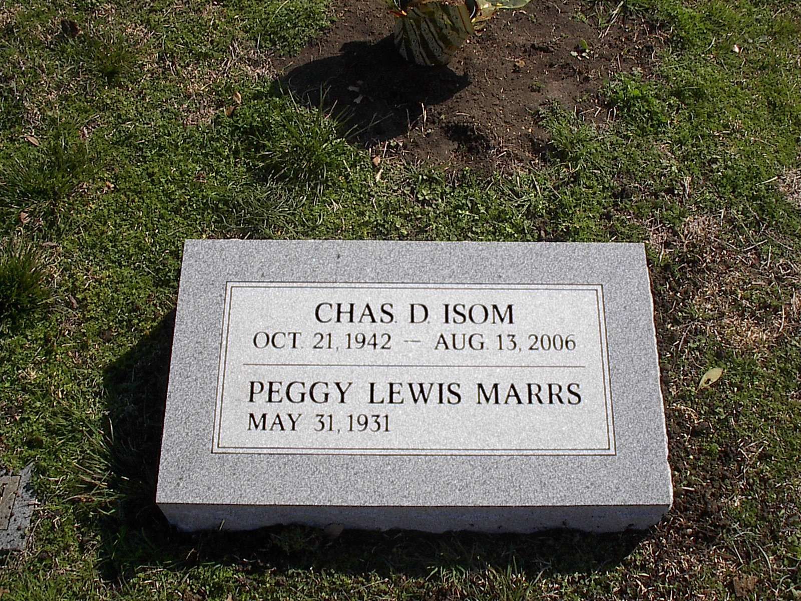 Gravestone of Chas D. Isom (Oct 21, 1942 - Aug 13, 2006) and Peggy Lewis Marrs (May 31, 1931) on green grass.