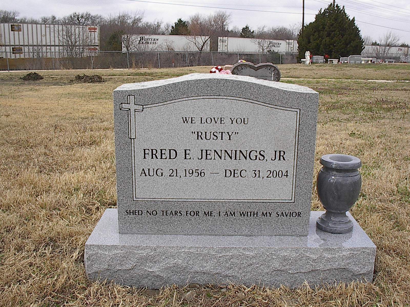 Gravestone of Fred E. Jennings Jr. in a cemetery. It has a cross, and an urn.