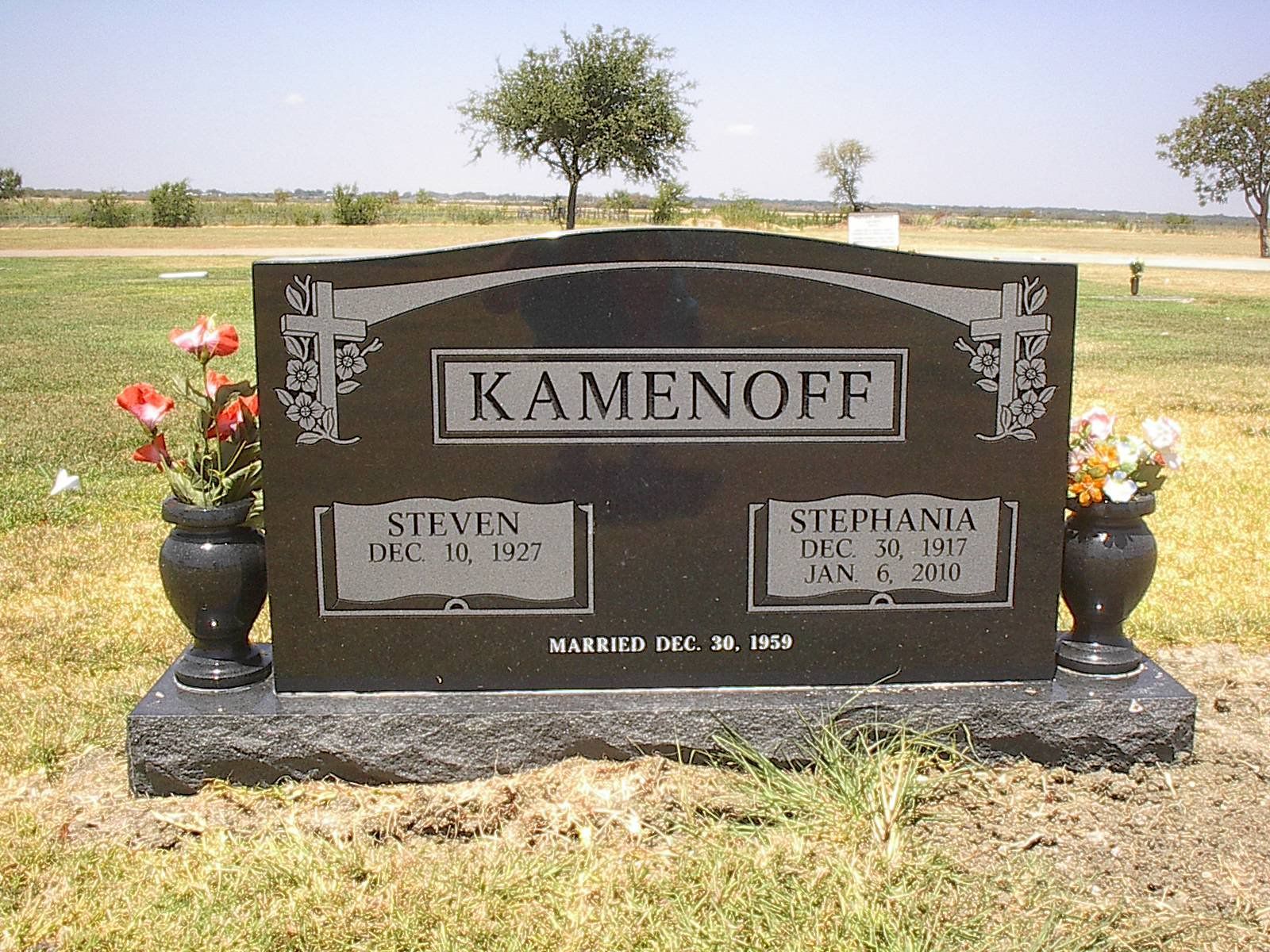 Black granite headstone for Kamenoff family with flowers, in a cemetery.