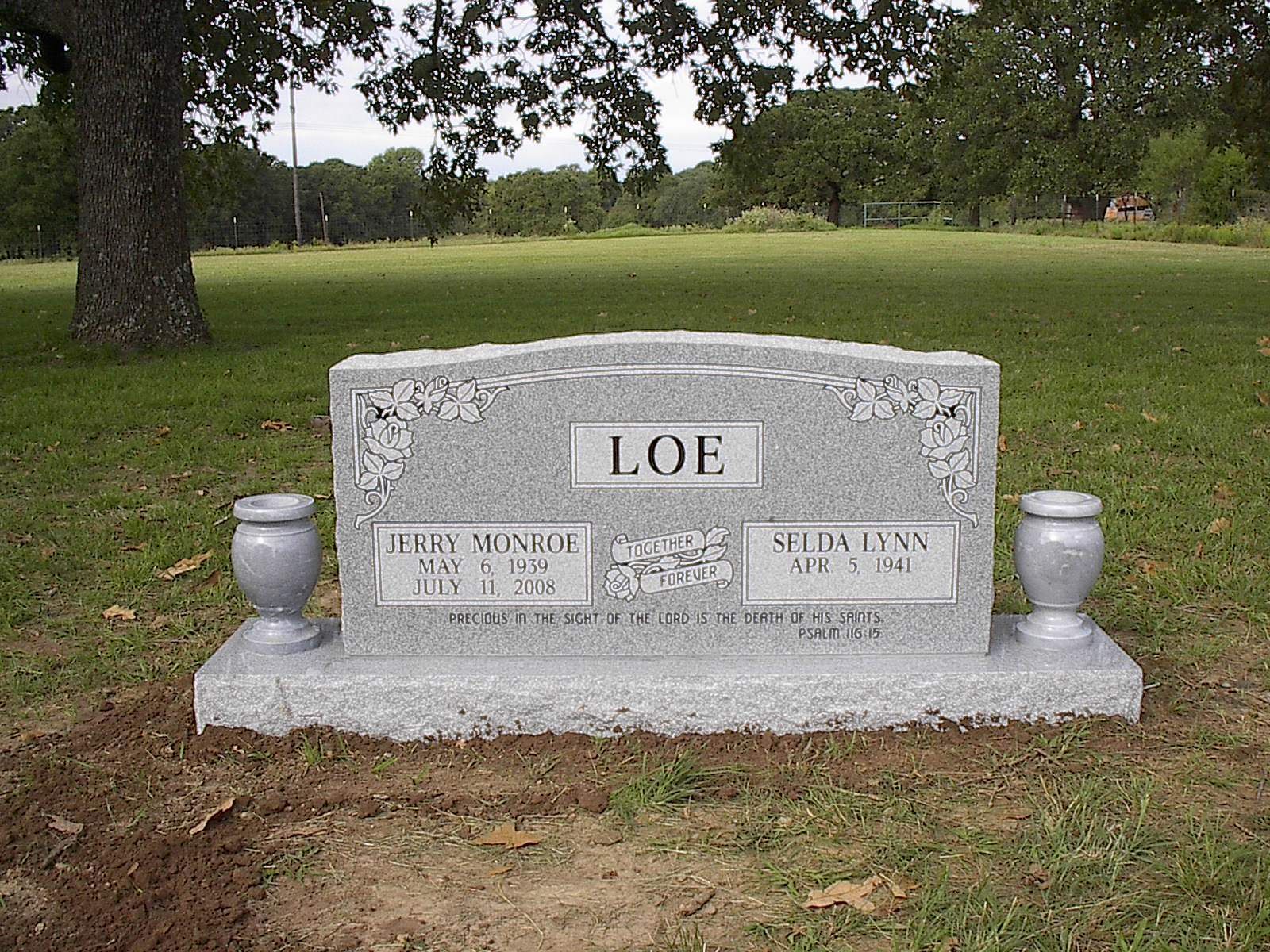 Gray headstone with the name LOE and two smaller sections for names and dates, in a grassy field.