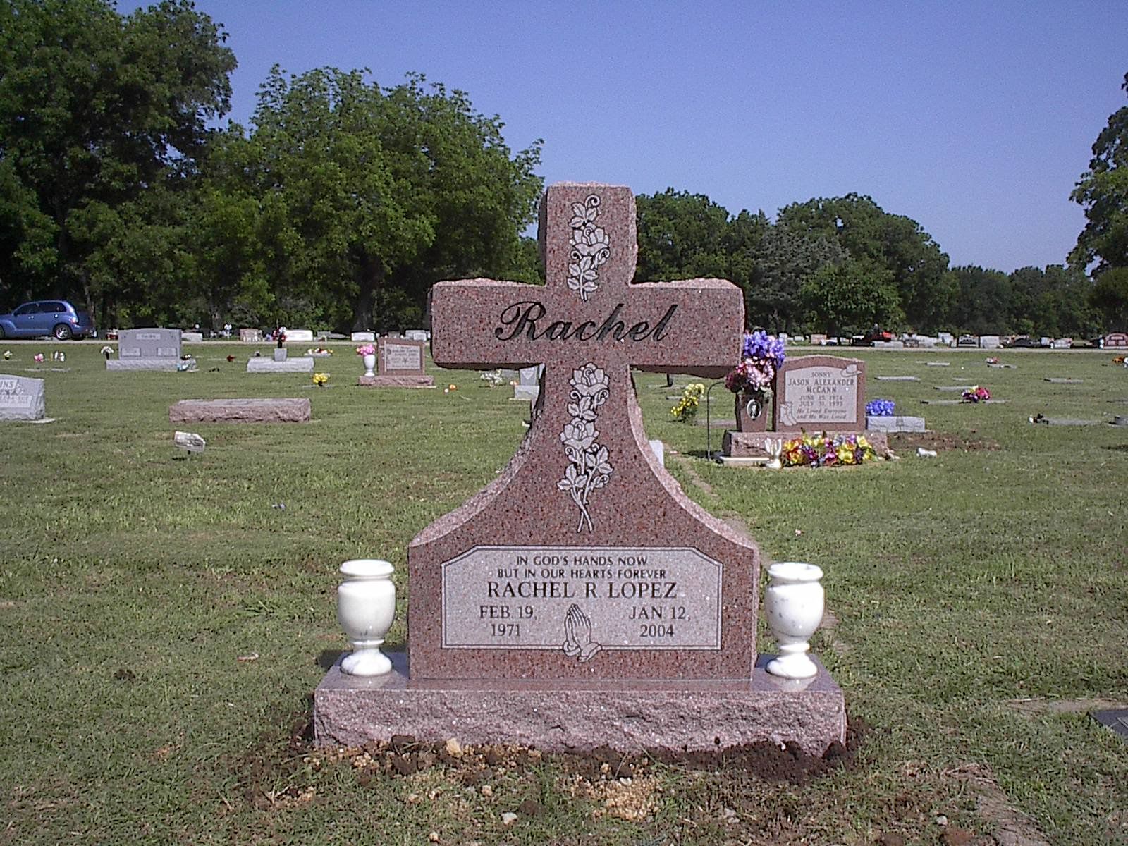 Gravestone in a cemetery, with a cross-shaped headstone that says 