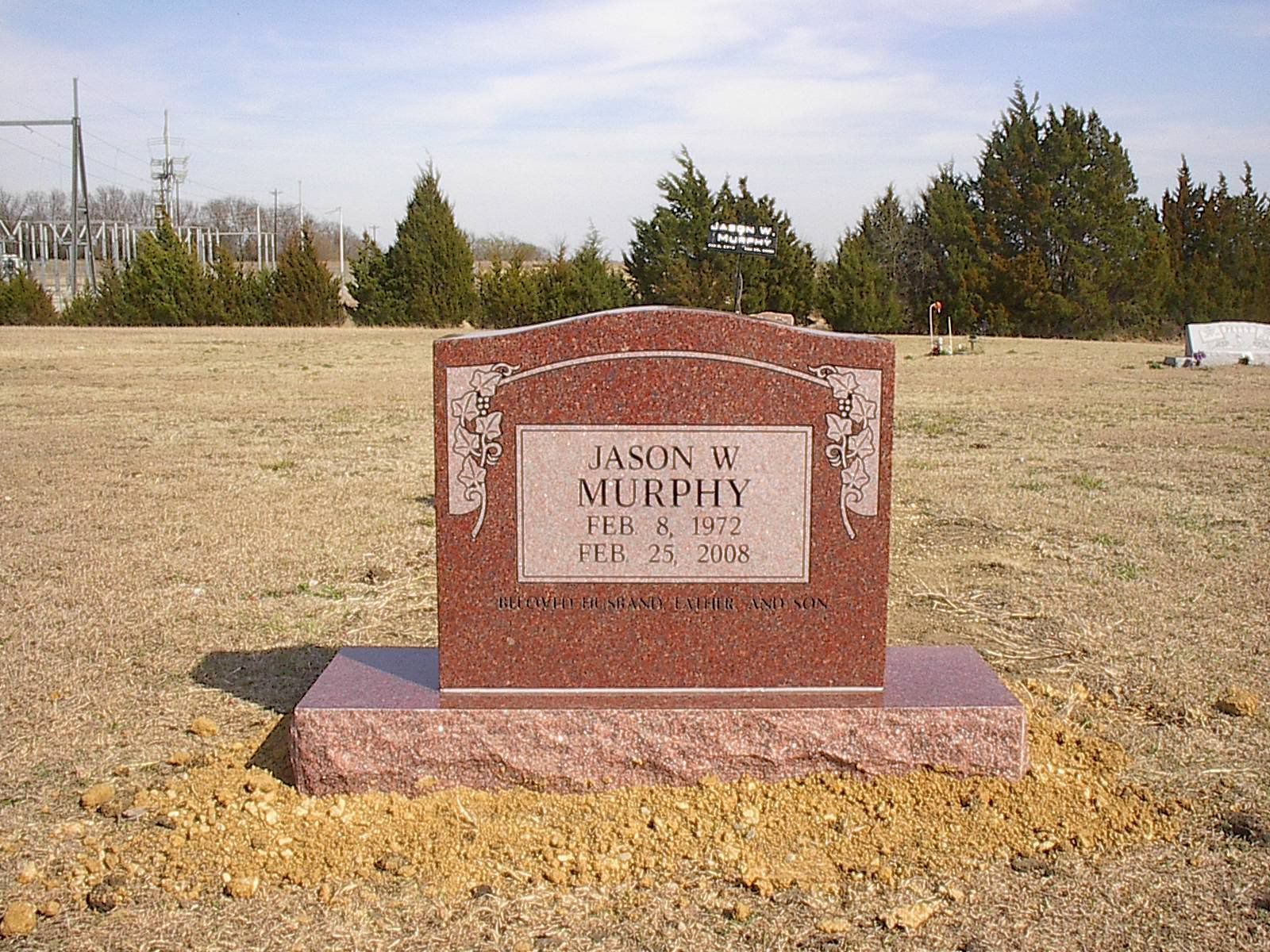 Red granite headstone in a grassy field; reads