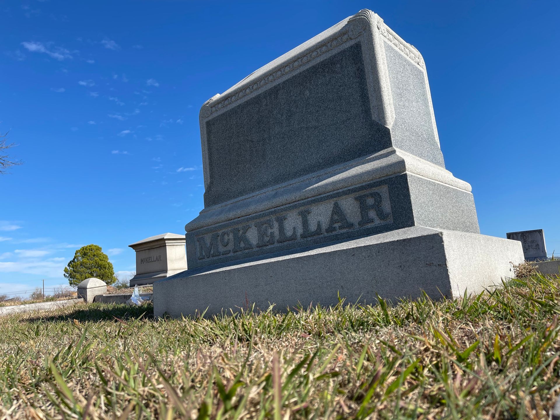 Gray gravestone in a grassy field against a blue sky, inscription 