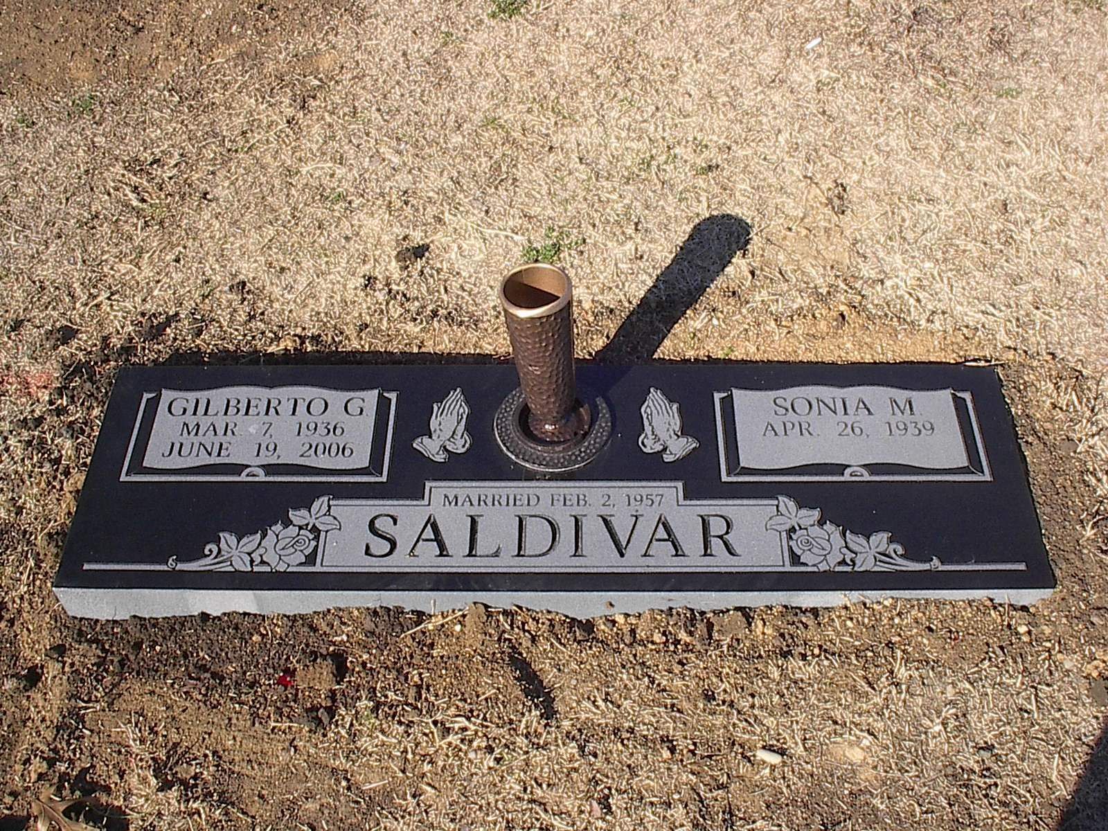 A black gravestone with the names Gilberto G. and Sonia M. Saldivar, dates of birth and death, and a central vase.
