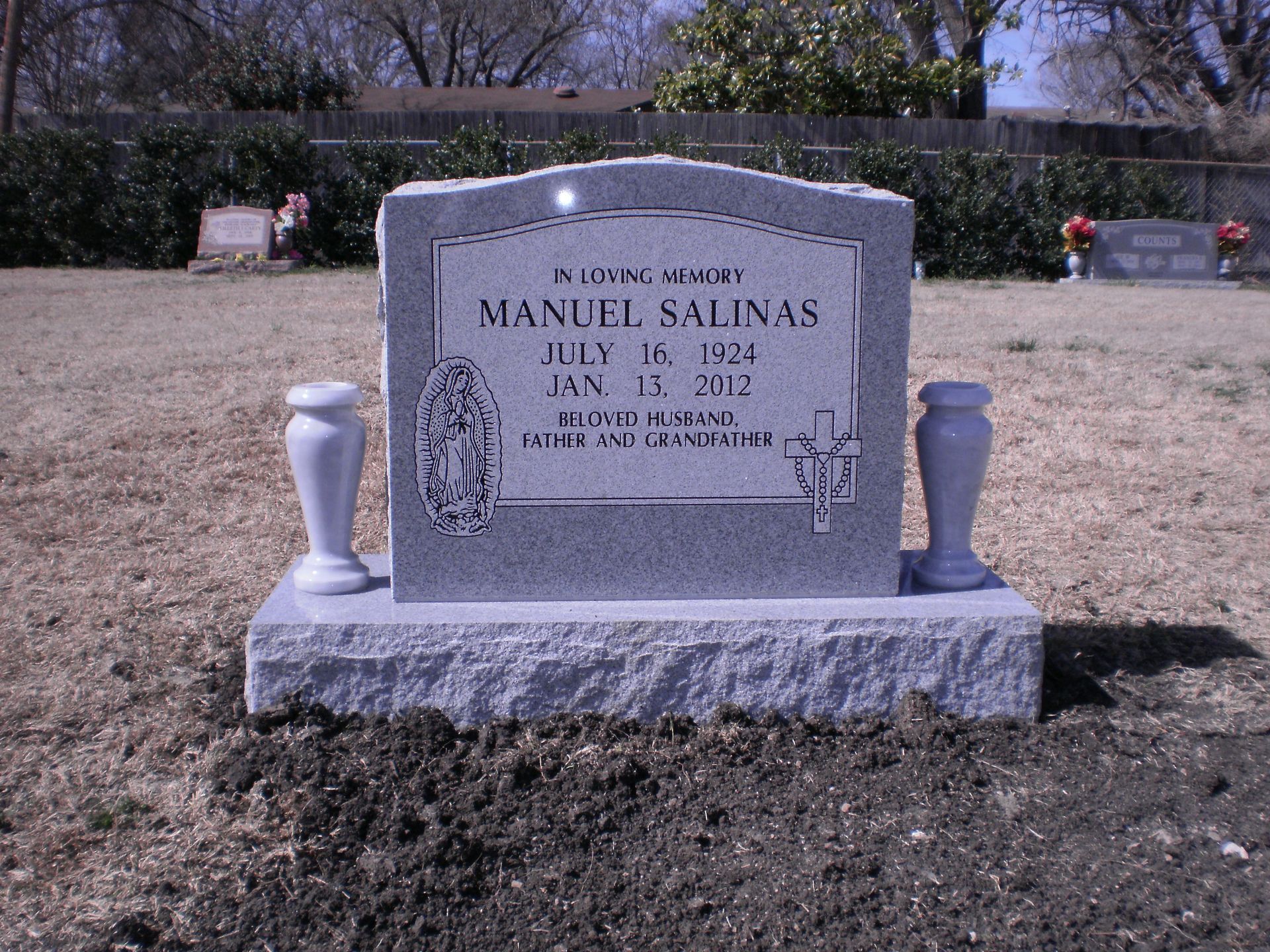Headstone of Manuel Salinas in a grassy cemetery. The headstone is gray with engraved text and design elements.