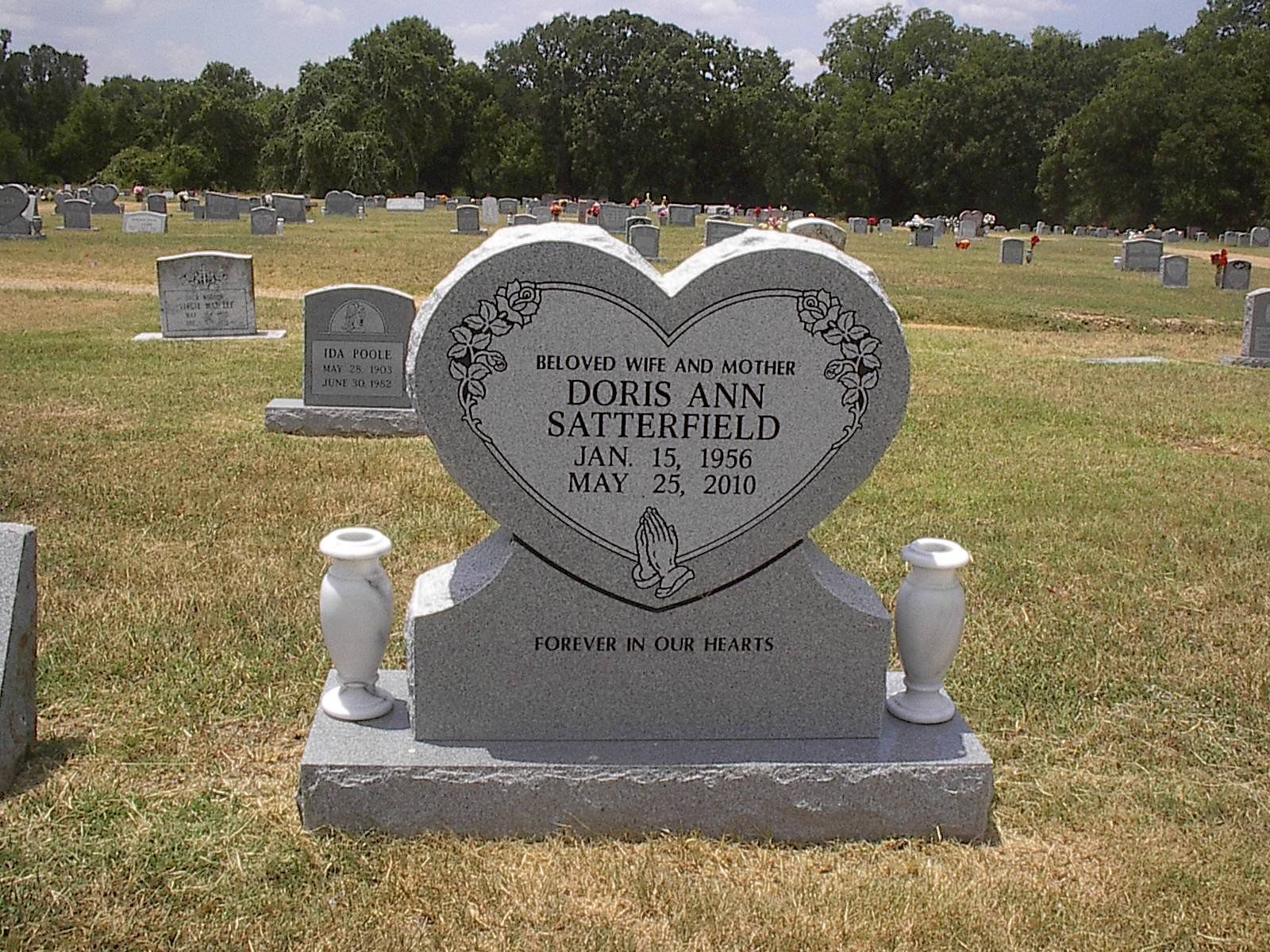 Heart-shaped tombstone with the name Doris Ann Satterfield and dates in a grassy cemetery. Two vases flank the stone.