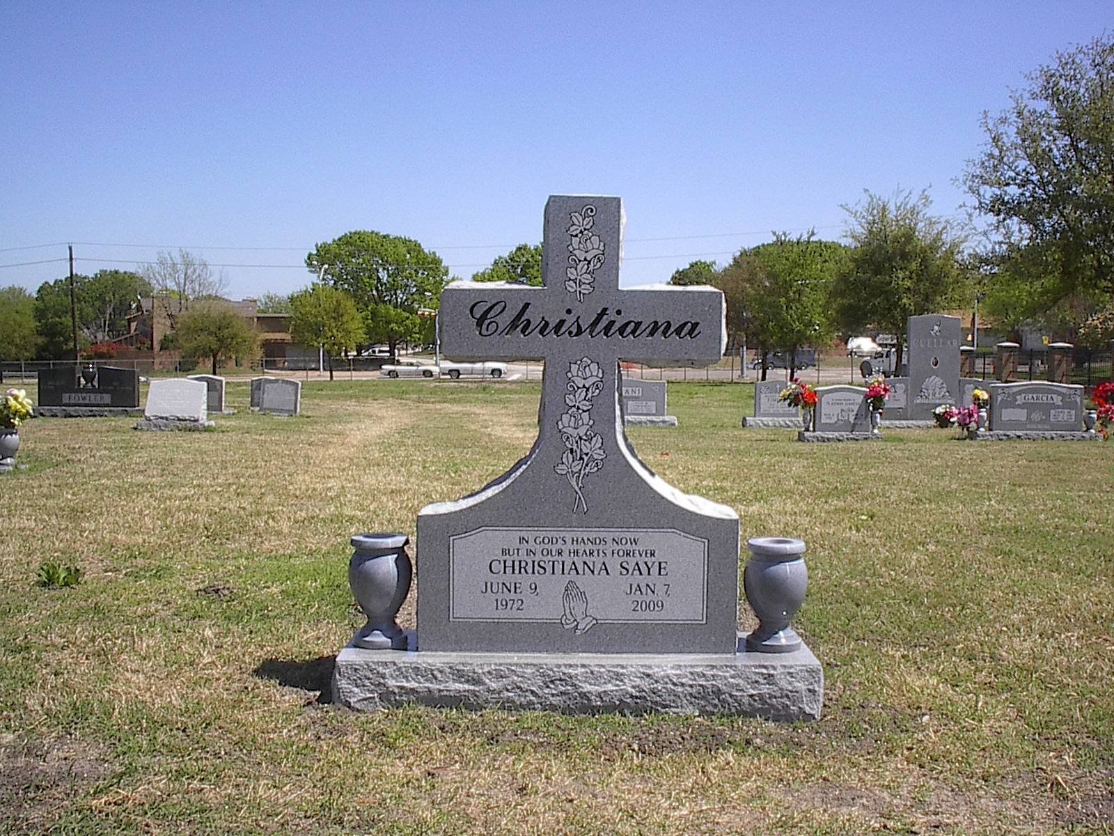 Gray cross-shaped gravestone in a cemetery, with the name 