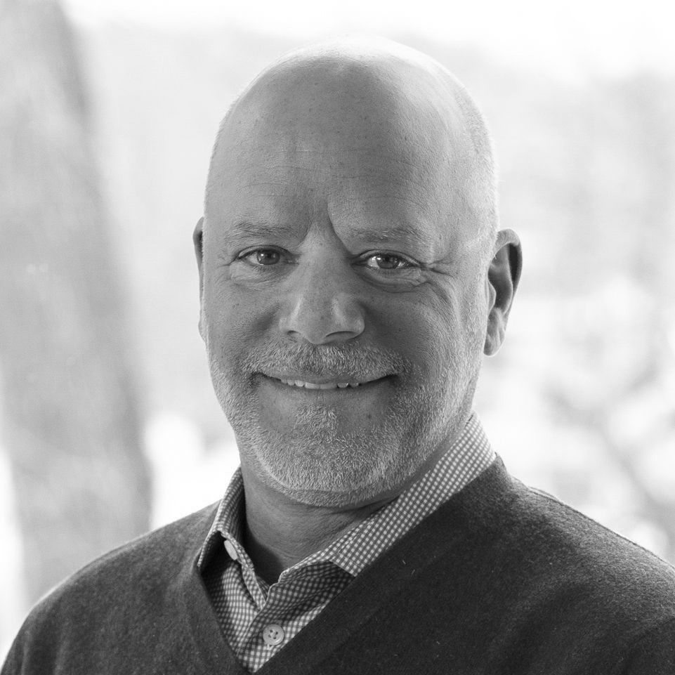 A man with a beard is smiling in a black and white photo. andy deckas