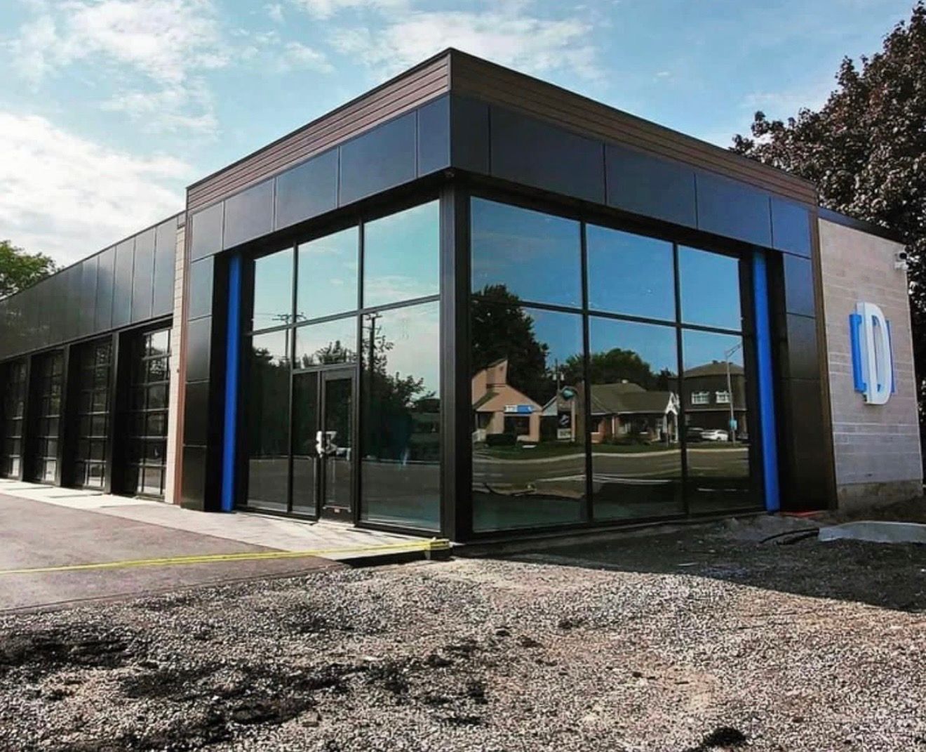 Bâtiment commercial moderne avec façade en verre, finitions noires et touches de bleu, sur un terrain en gravier.