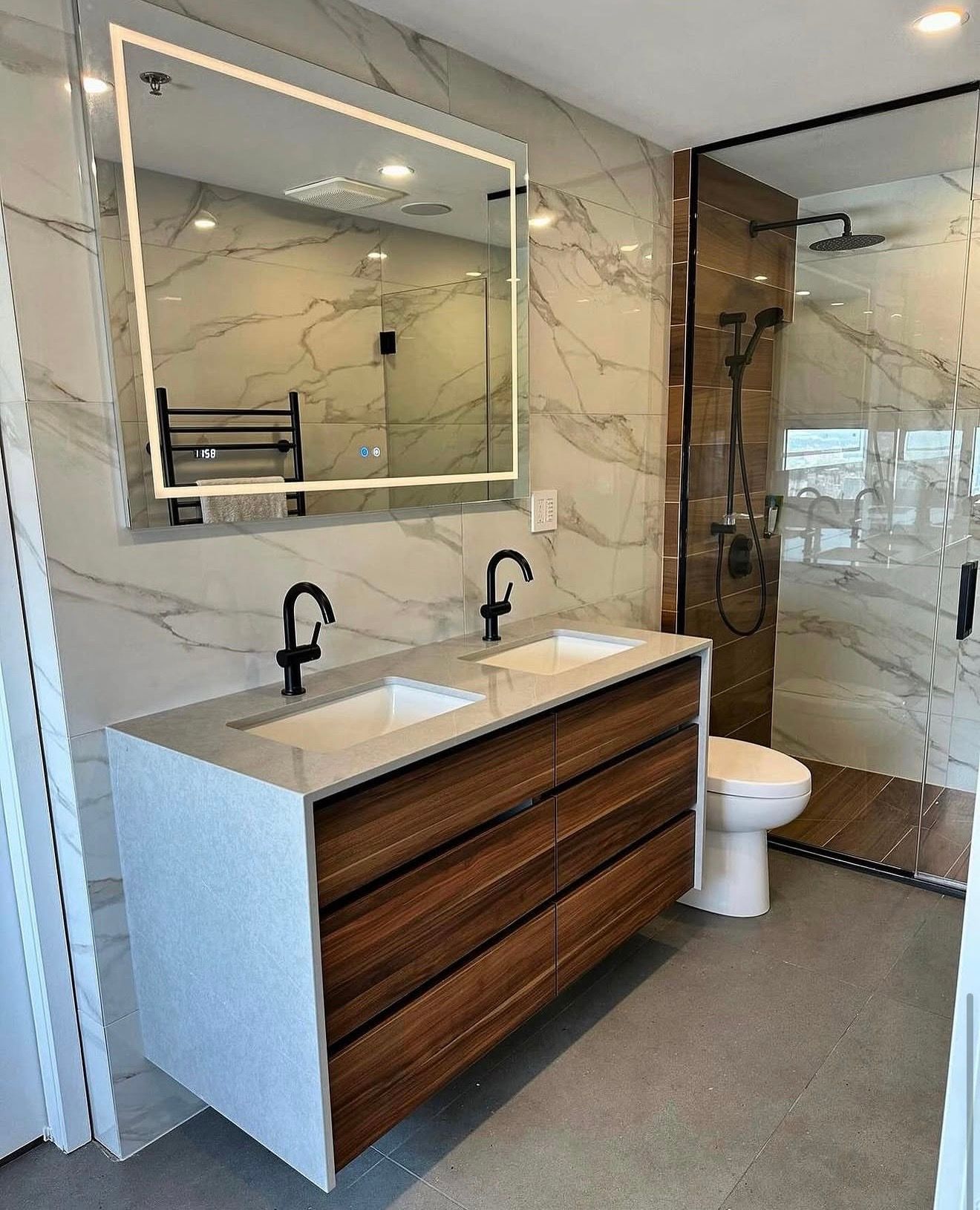 Salle de bain avec double lavabo en bois, miroir &eacute;clair&eacute;, carrelage marbre et douche vitr&eacute;e.