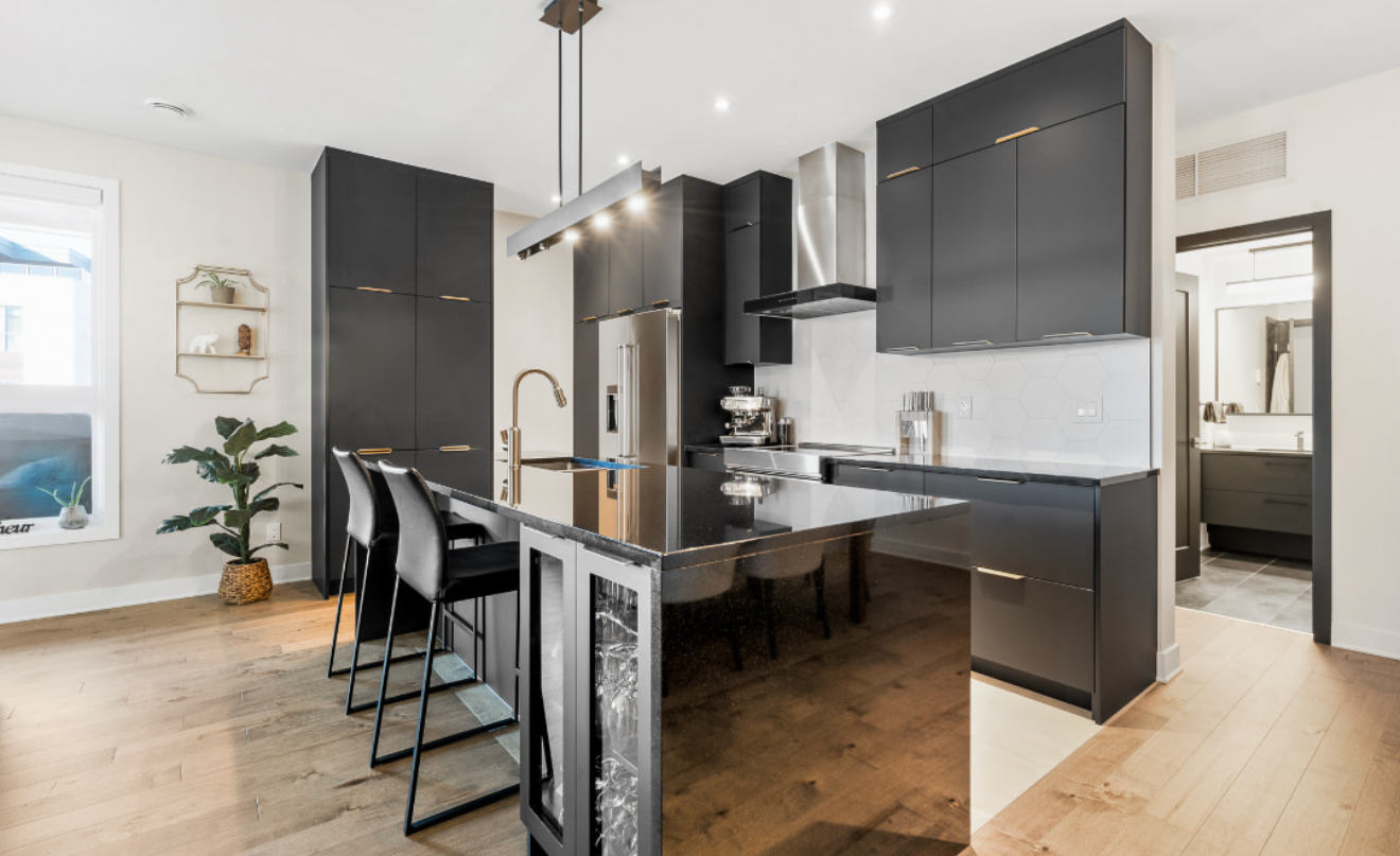 Cuisine moderne avec armoires foncées, îlot central avec coin repas, électroménagers en acier inoxydable et parquet.